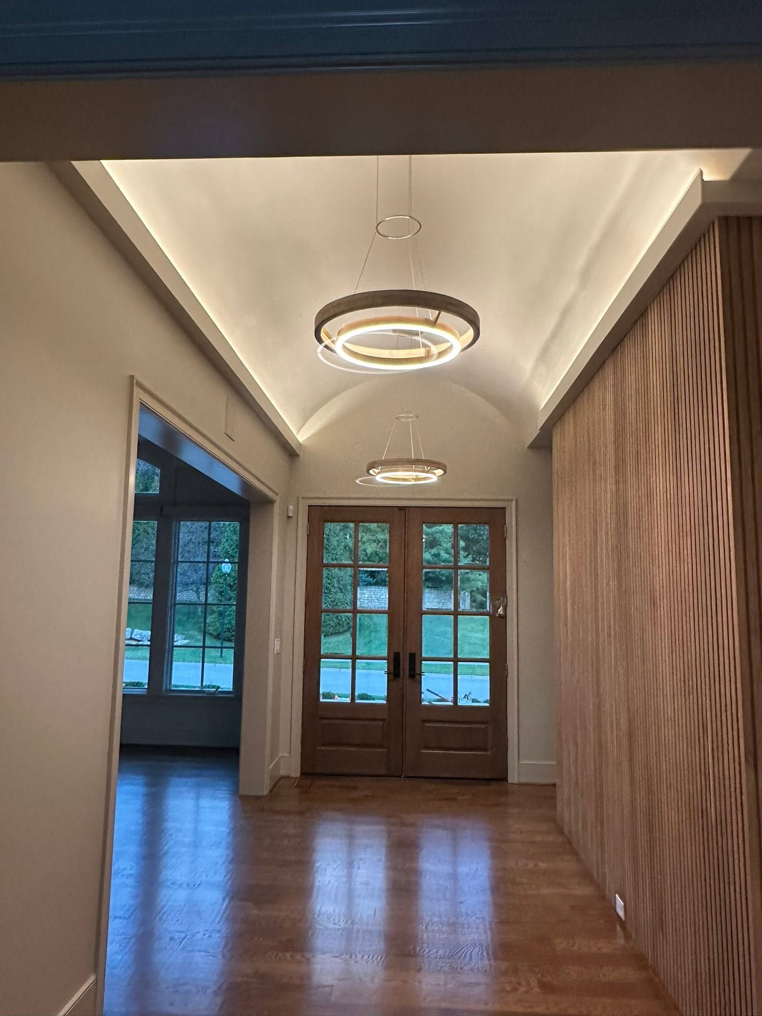 Empty hallway with polished wood floors, modern ceiling lights, and glass double doors at the far end.
