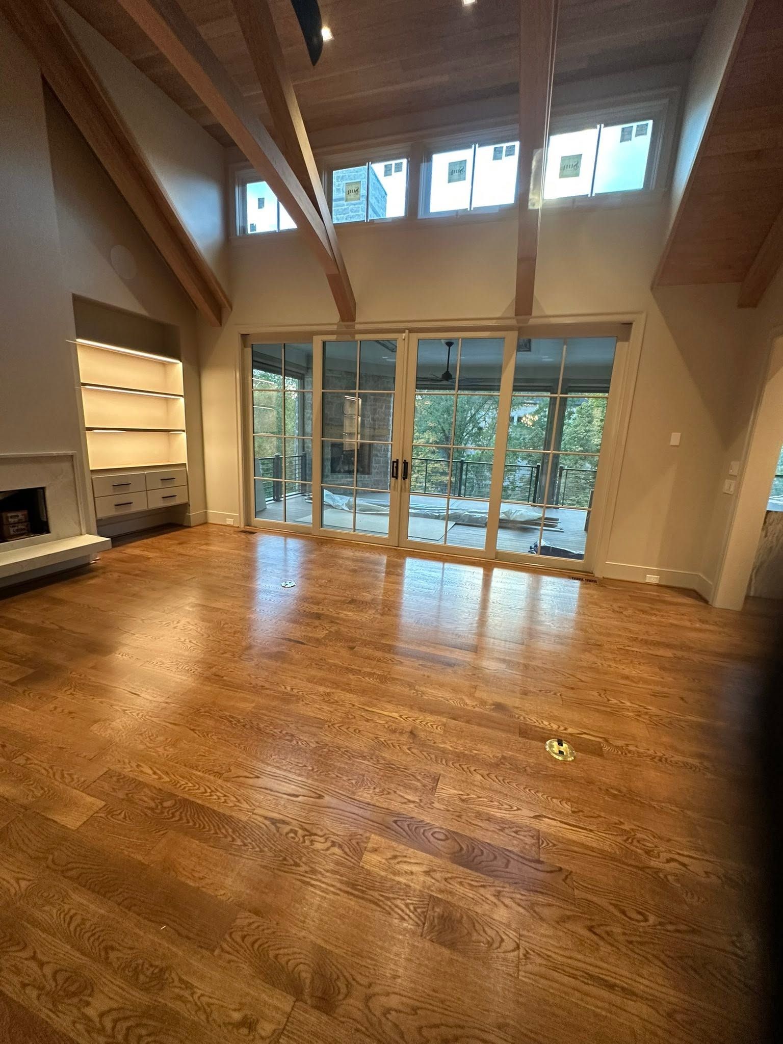 Spacious living room with vaulted ceiling, hardwood floors, and glass doors opening to a wooded patio.