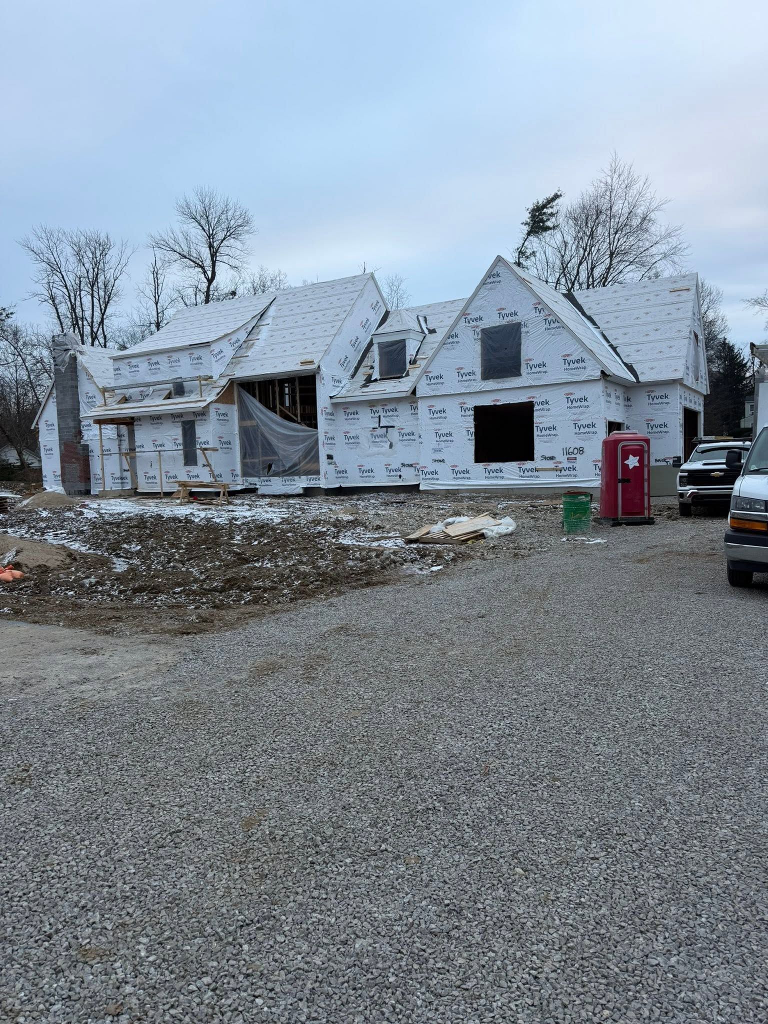 Partially built house with white sheathing, gravel driveway, and a red portable toilet in front