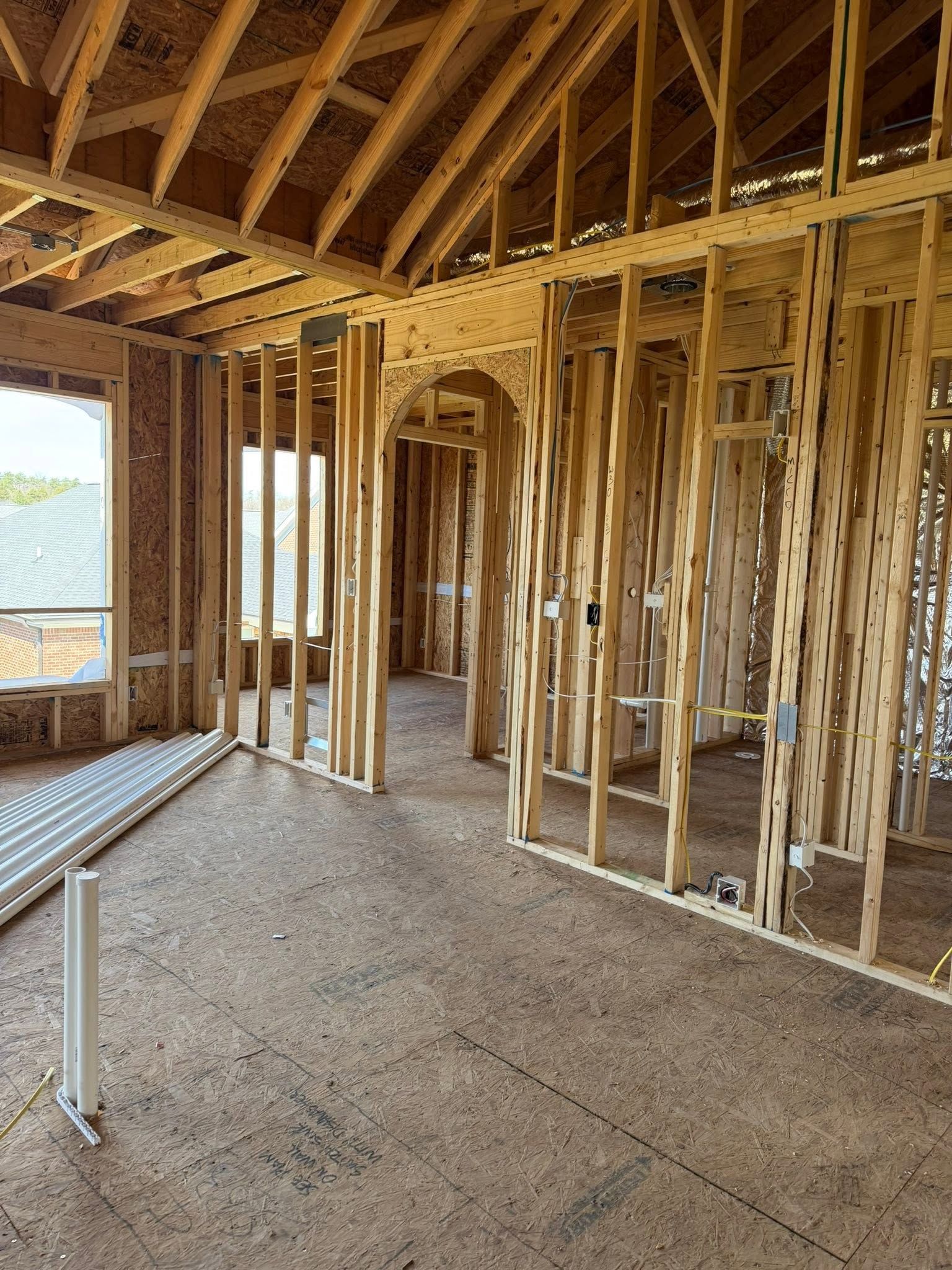 Framed house interior under construction with exposed wood studs and roof trusses, gravel floor, and window opening