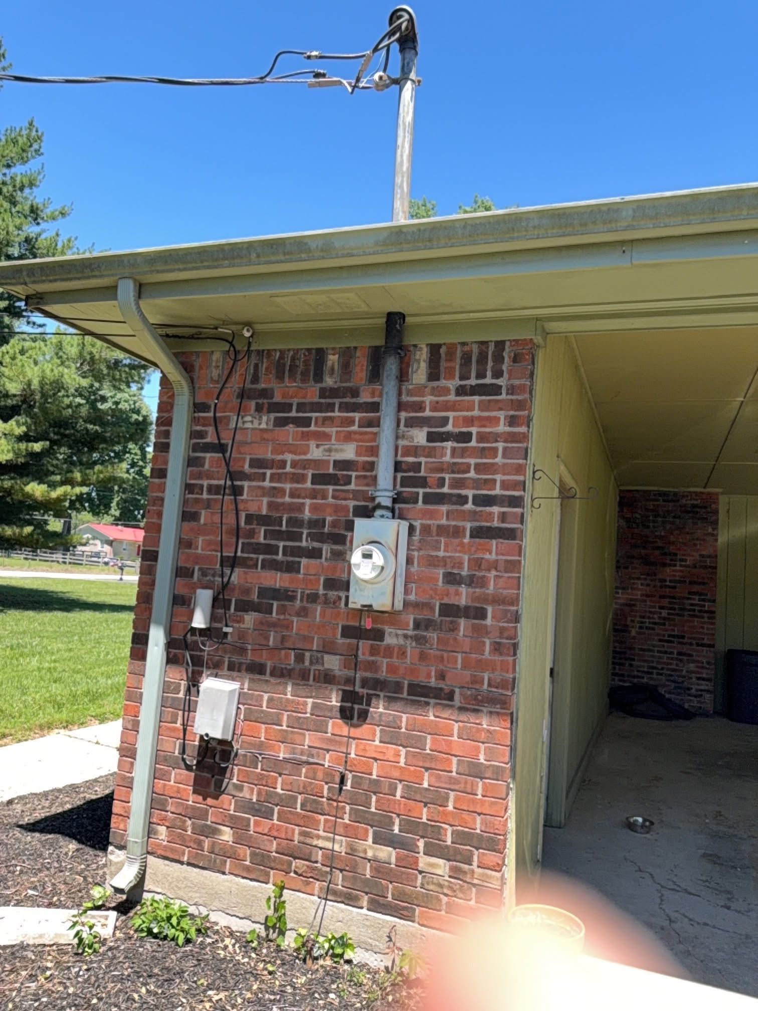 Brick building exterior with utility meter, wires, and an open carport or walkway.