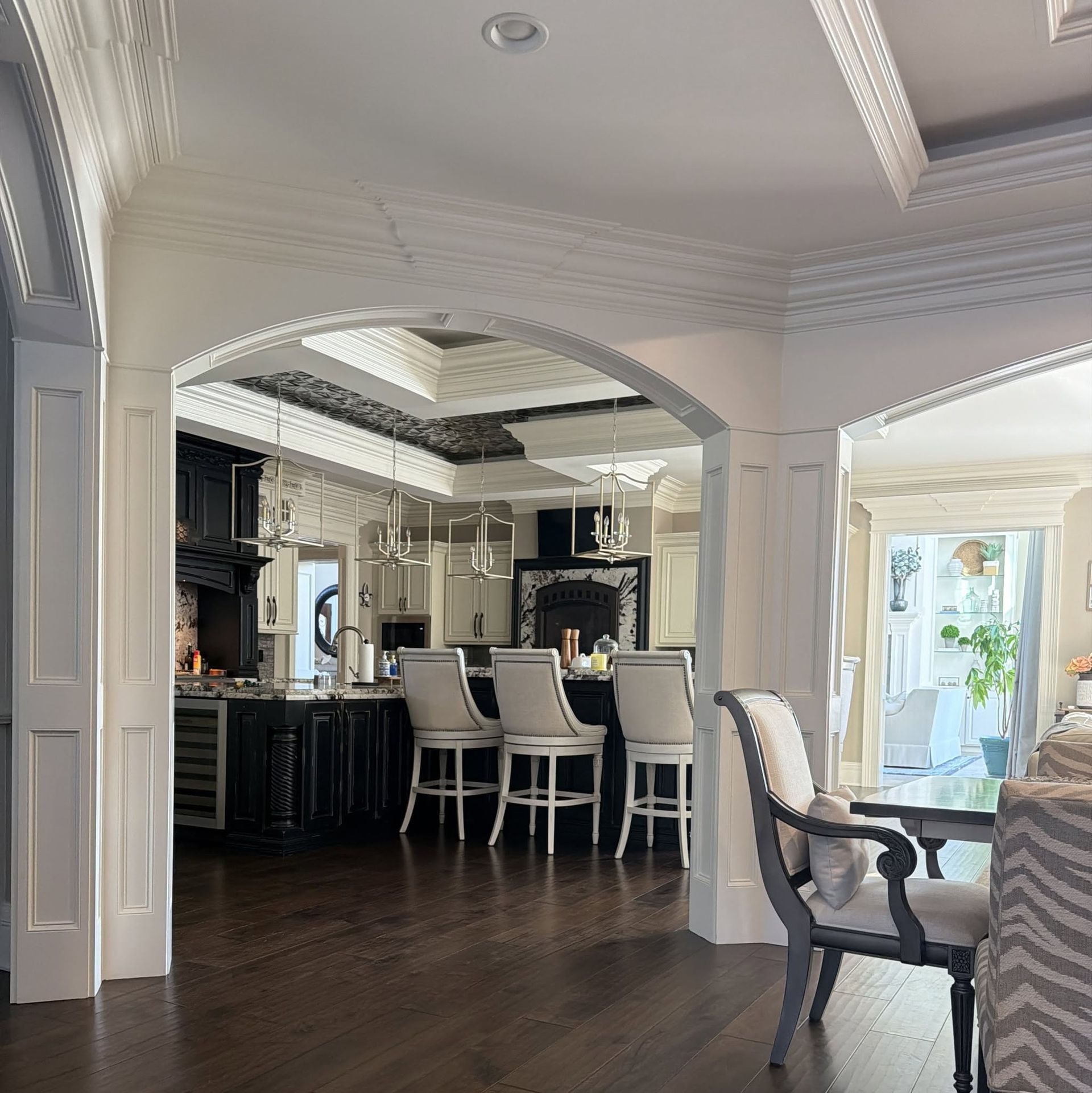 Elegant open-concept kitchen and dining area with white chairs, dark wood floors, and ornate molding