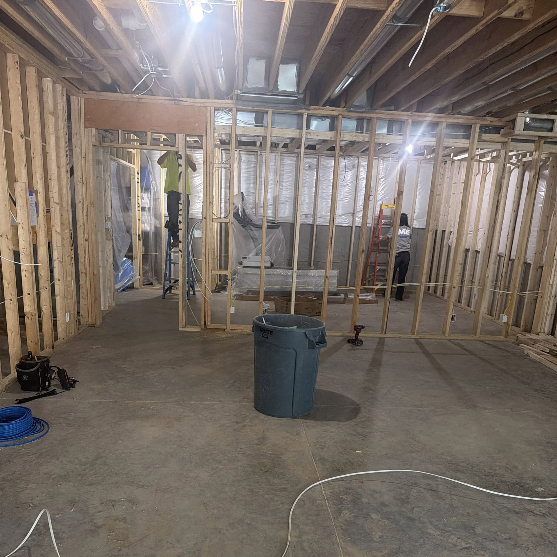 Unfinished basement with exposed framing, concrete floor, trash can, and scattered tools under construction