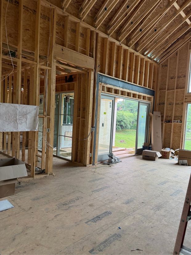 Unfinished room with exposed wooden framing, open doorway, and construction materials on the floor.