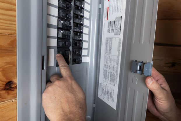 Hands adjusting circuit breakers in an open electrical panel box.