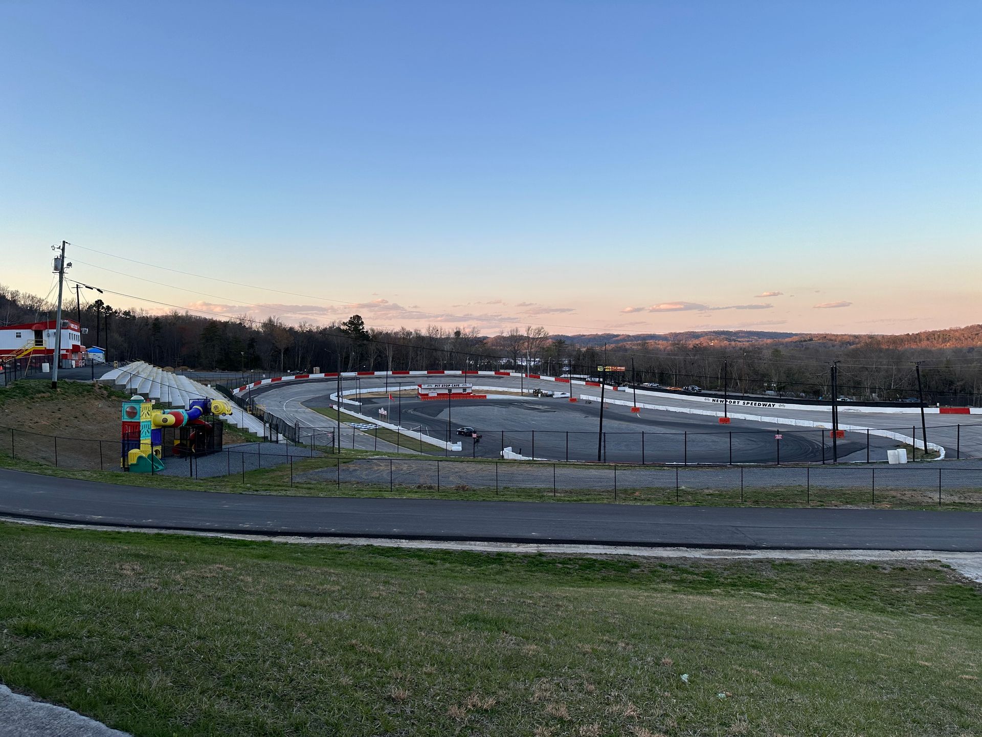 Outdoor racetrack at dusk with curving track, colorful tents, and grassy foreground under a clear sky