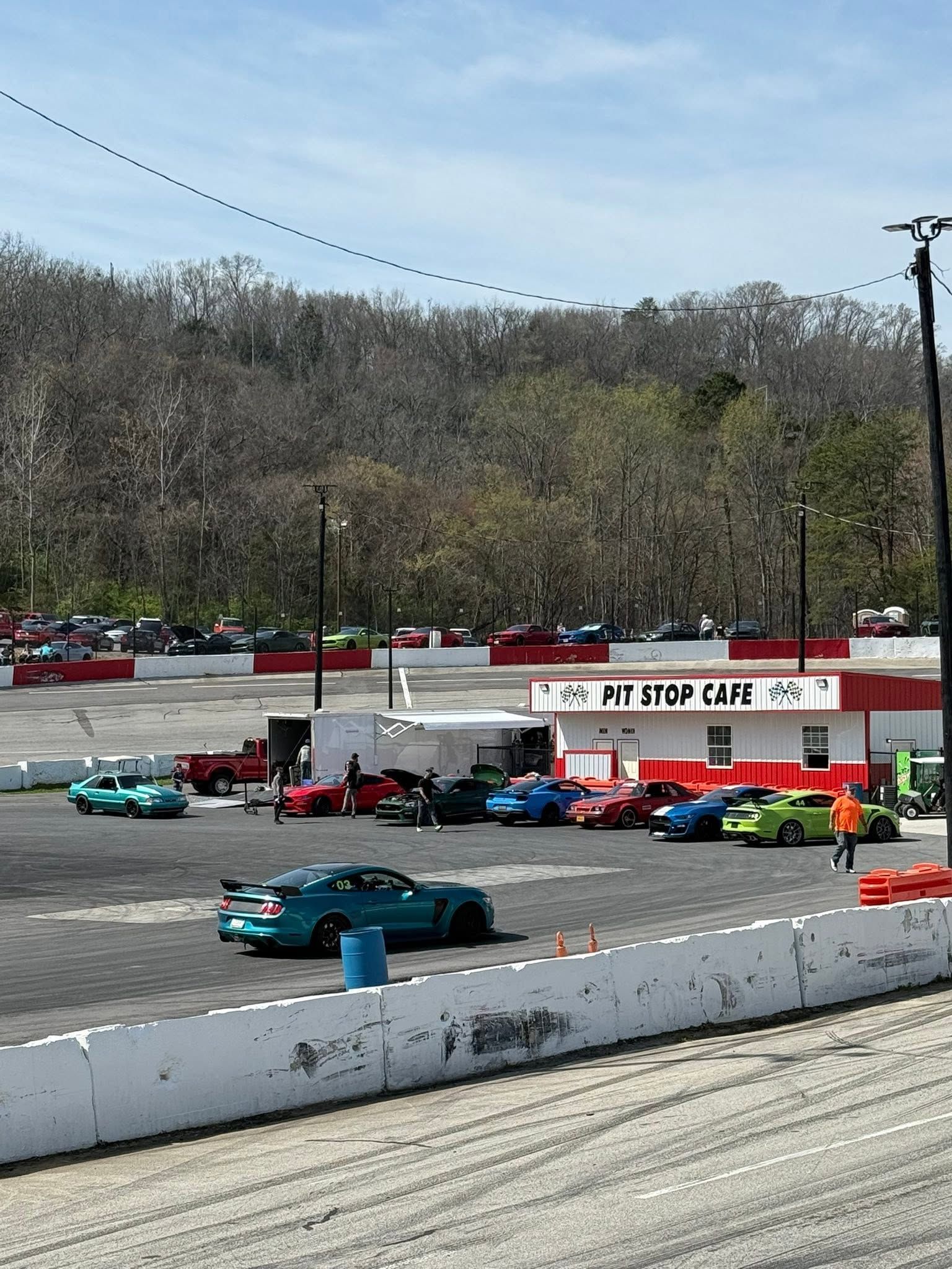 Stock car race on an oval track with colorful cars and a white barrier under a clear sky.