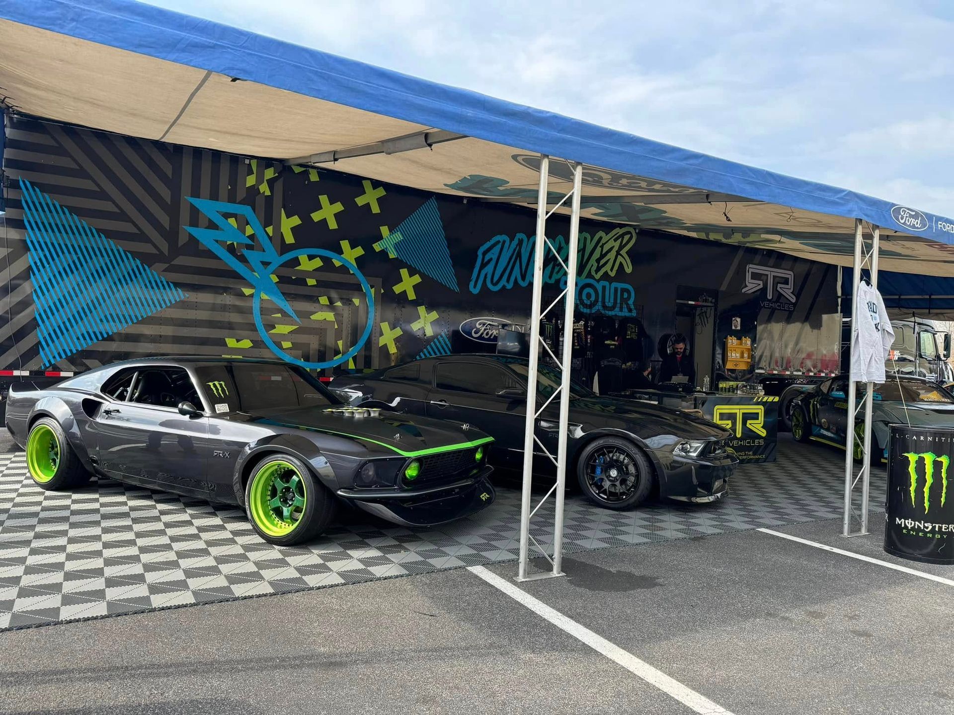 Two modified cars under a canopy at an outdoor auto show, one black with neon green rims.