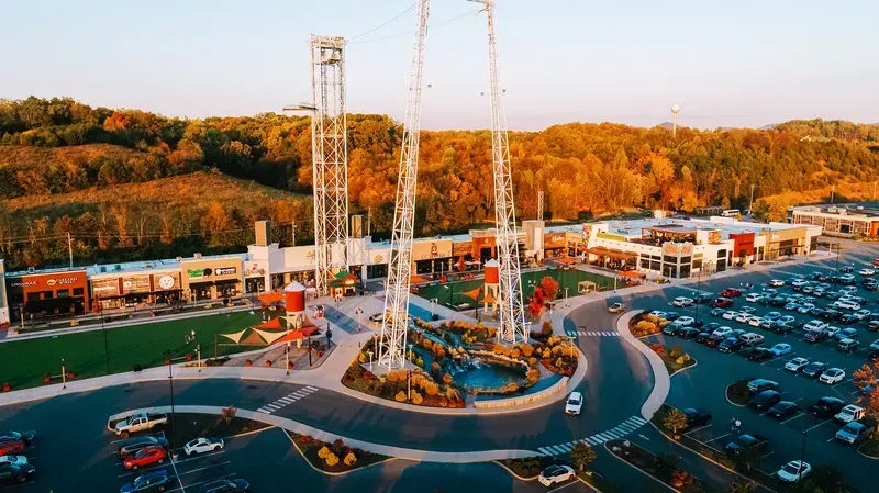 Aerial view of a theme park with a central ride, parking lot, and autumn trees at sunset