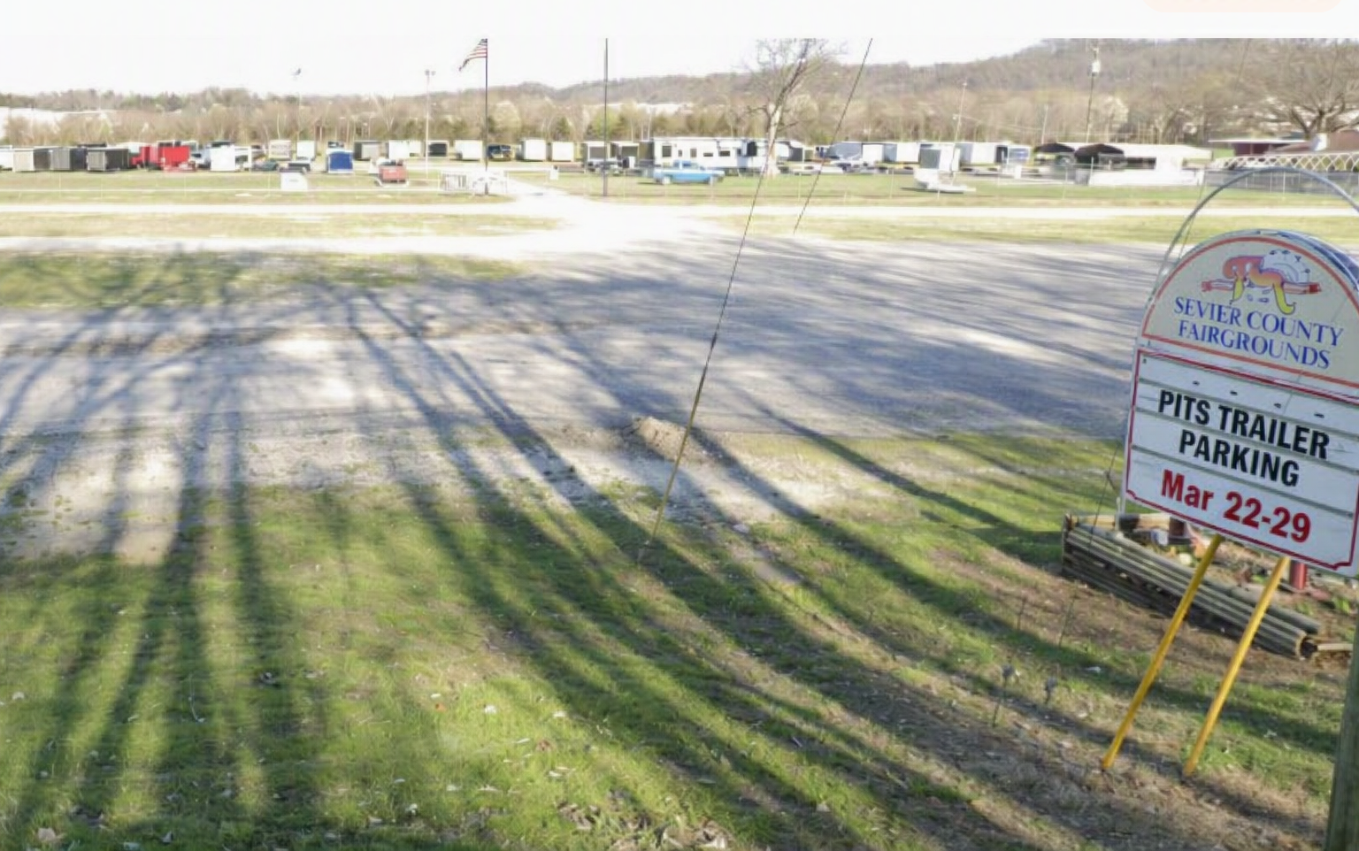 Vacant grassy lot with long tree shadows and a roadside sign advertising trailer parking spaces.