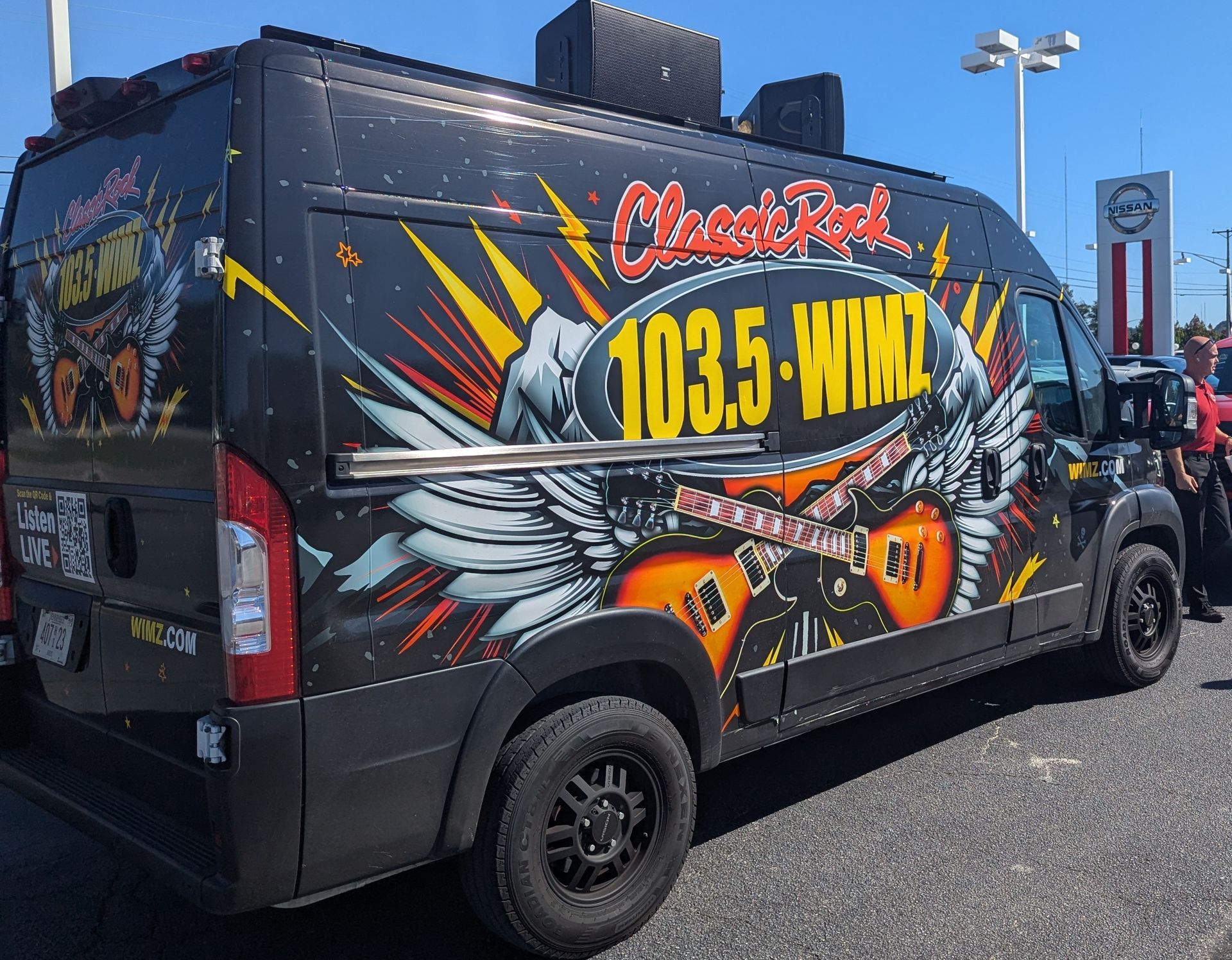 Wrapped black radio van with colorful “Classic Rock 103.5-WIMI” graphics parked outdoors