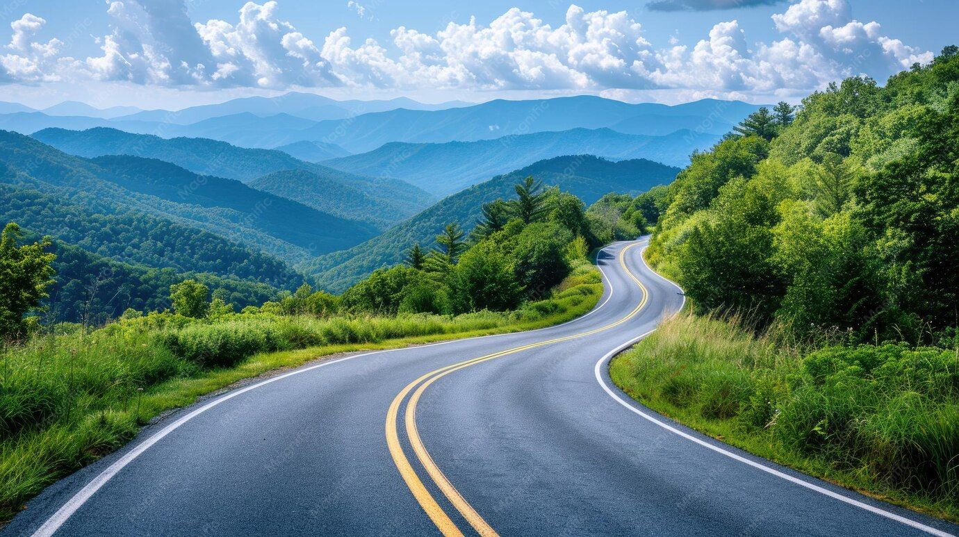 Winding mountain road through green hills under a blue sky with clouds