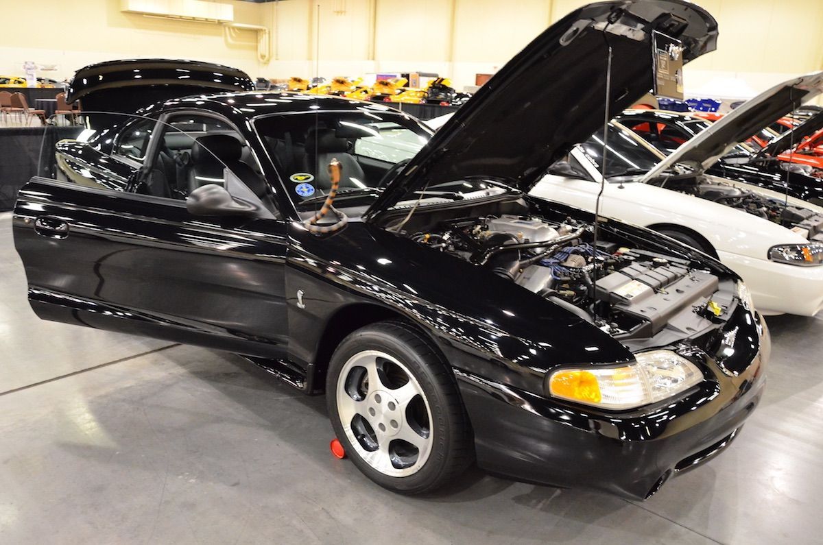 Black sports coupe with hood open on display in an indoor showroom.