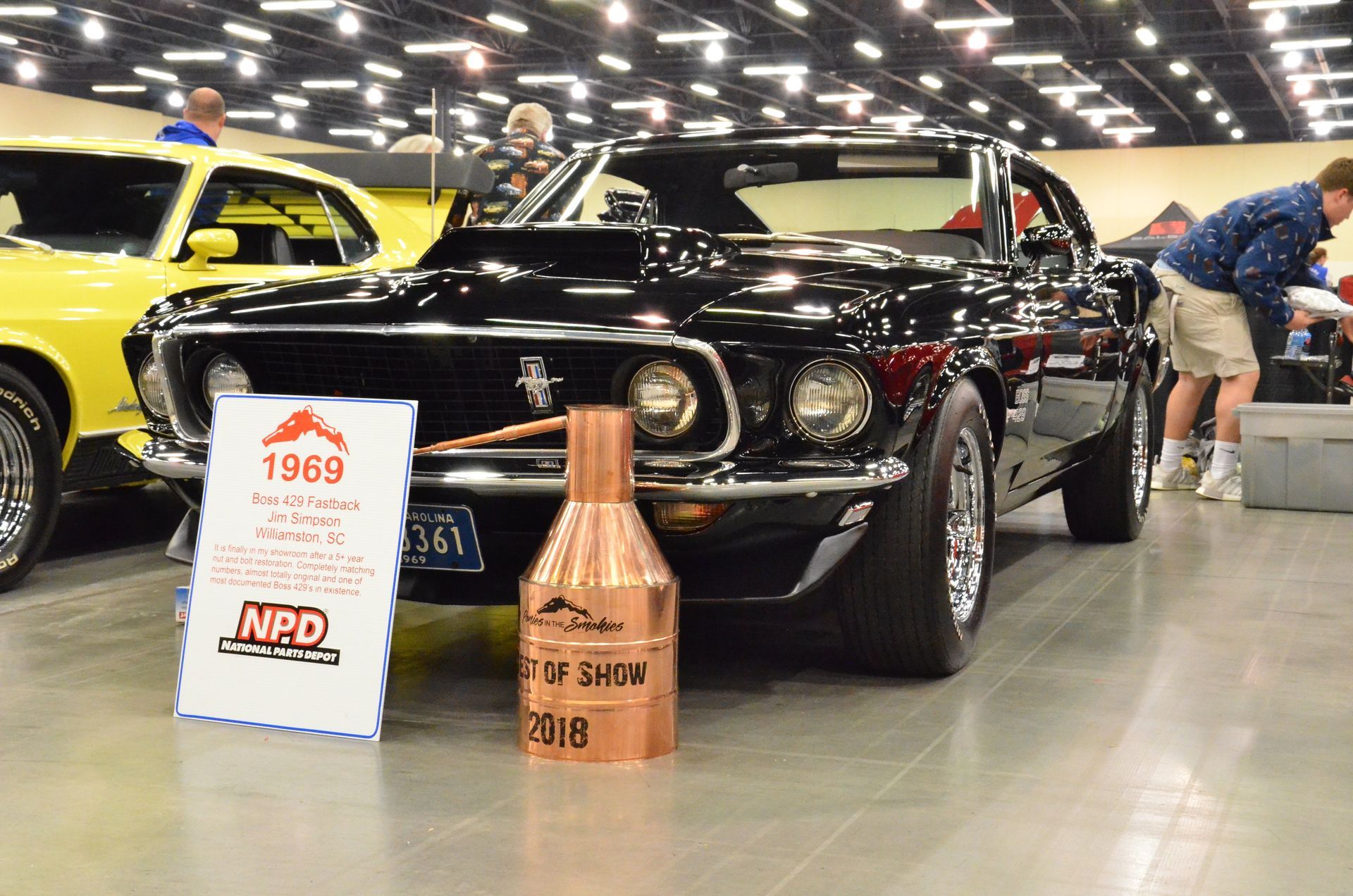 Black classic car displayed at an indoor car show with a 1969 sign and copper trophy plaque in front