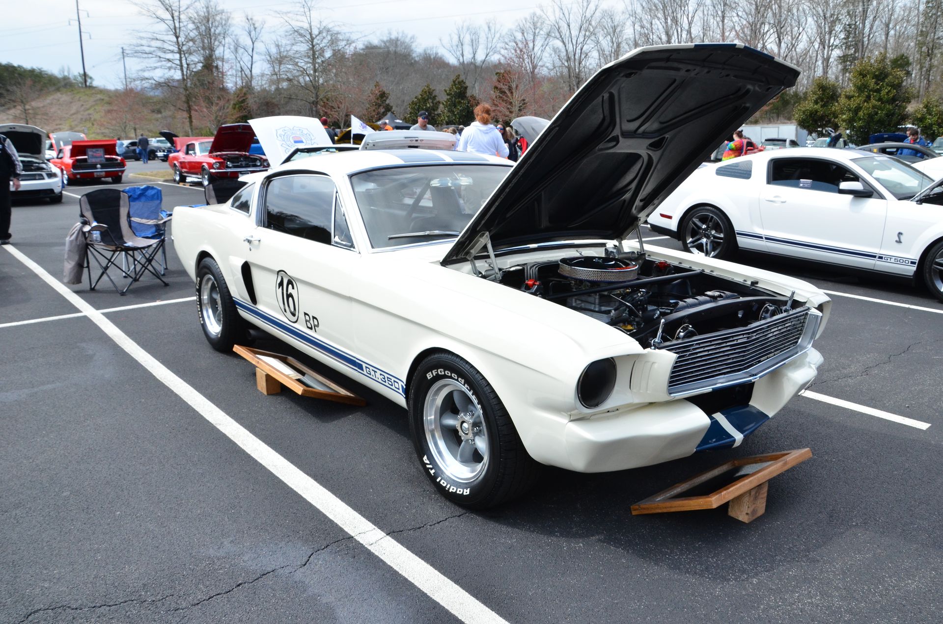 White classic Mustang with hood open at a car show, parked among other cars on a lot