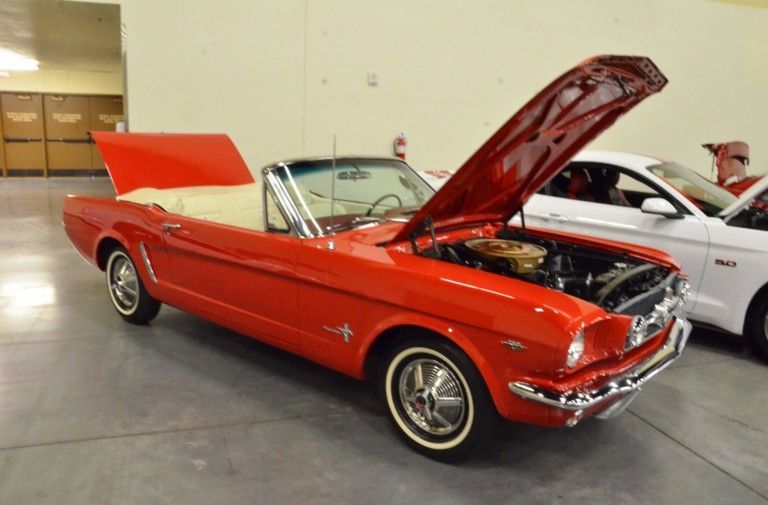 Red classic Ford Mustang convertible with hood open at an indoor car show
