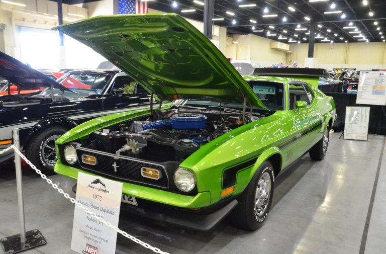 Bright lime-green classic muscle car on display indoors with hood open at an auto show.