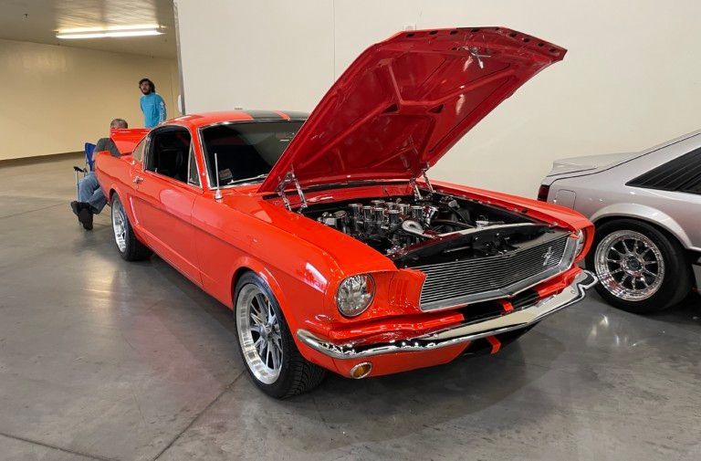 Red classic muscle car with hood open, displayed indoors at a car show.