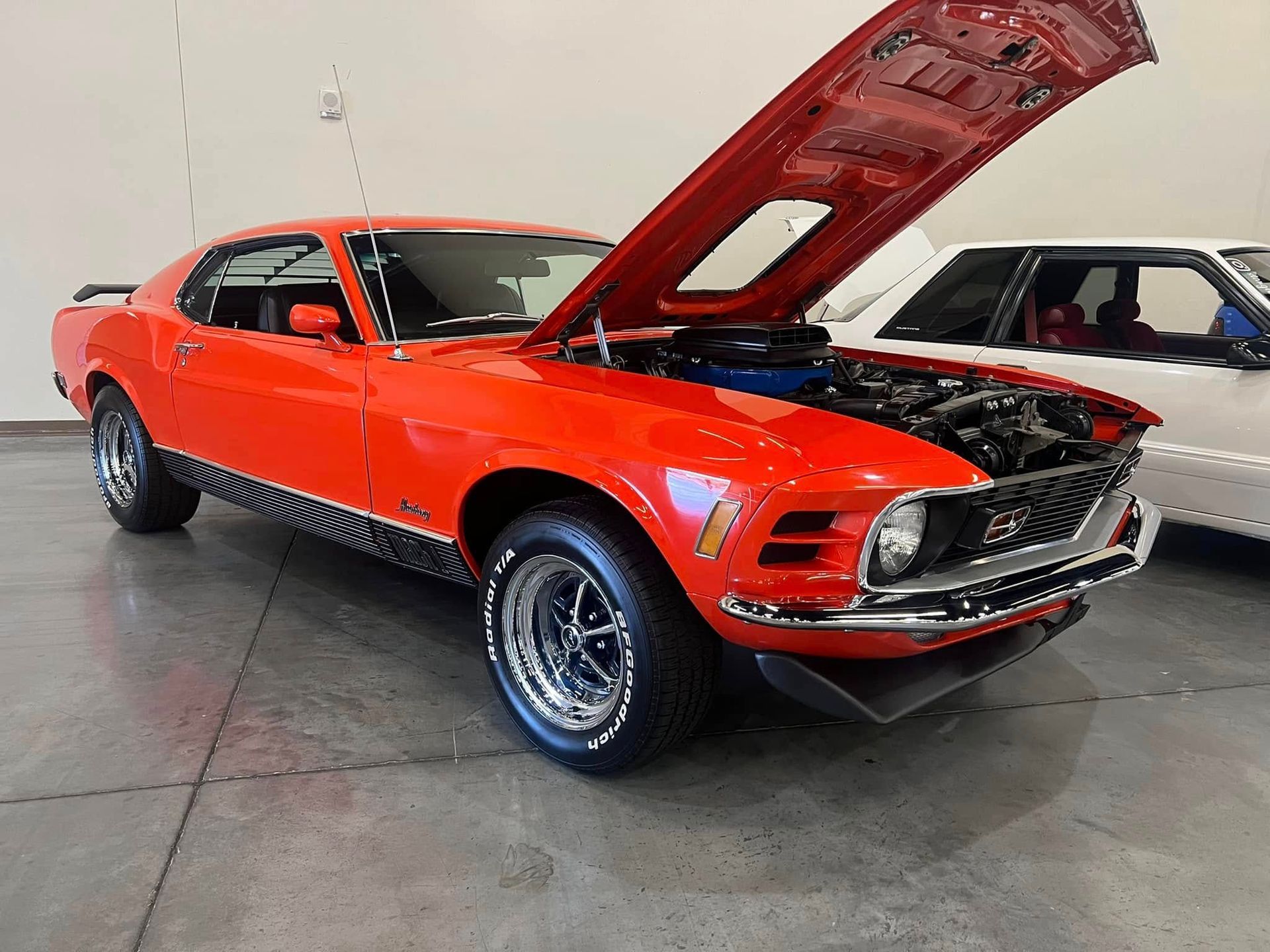 Red classic Ford Mustang with hood open on display in a showroom