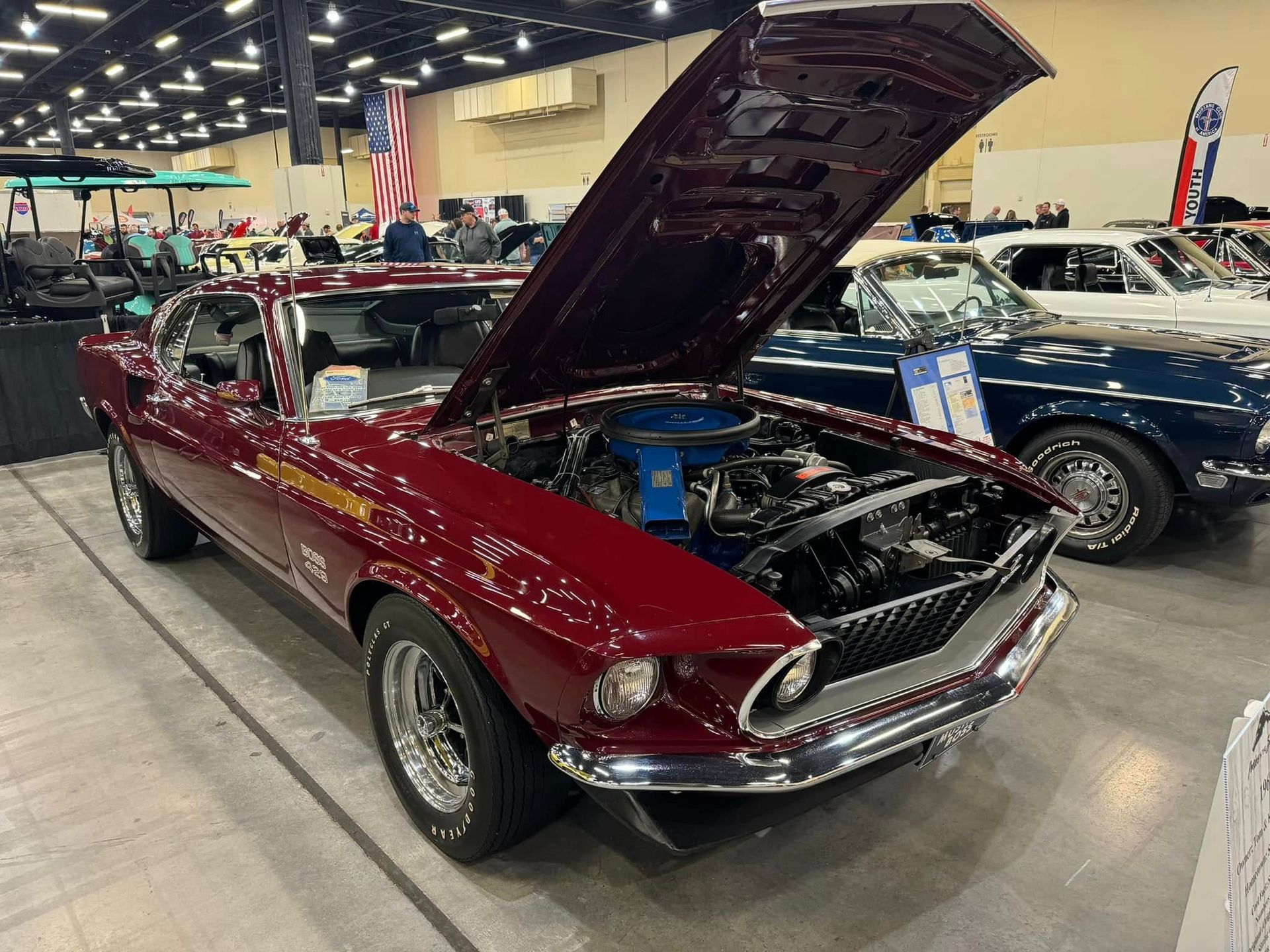 Maroon classic convertible with hood open at an indoor car show