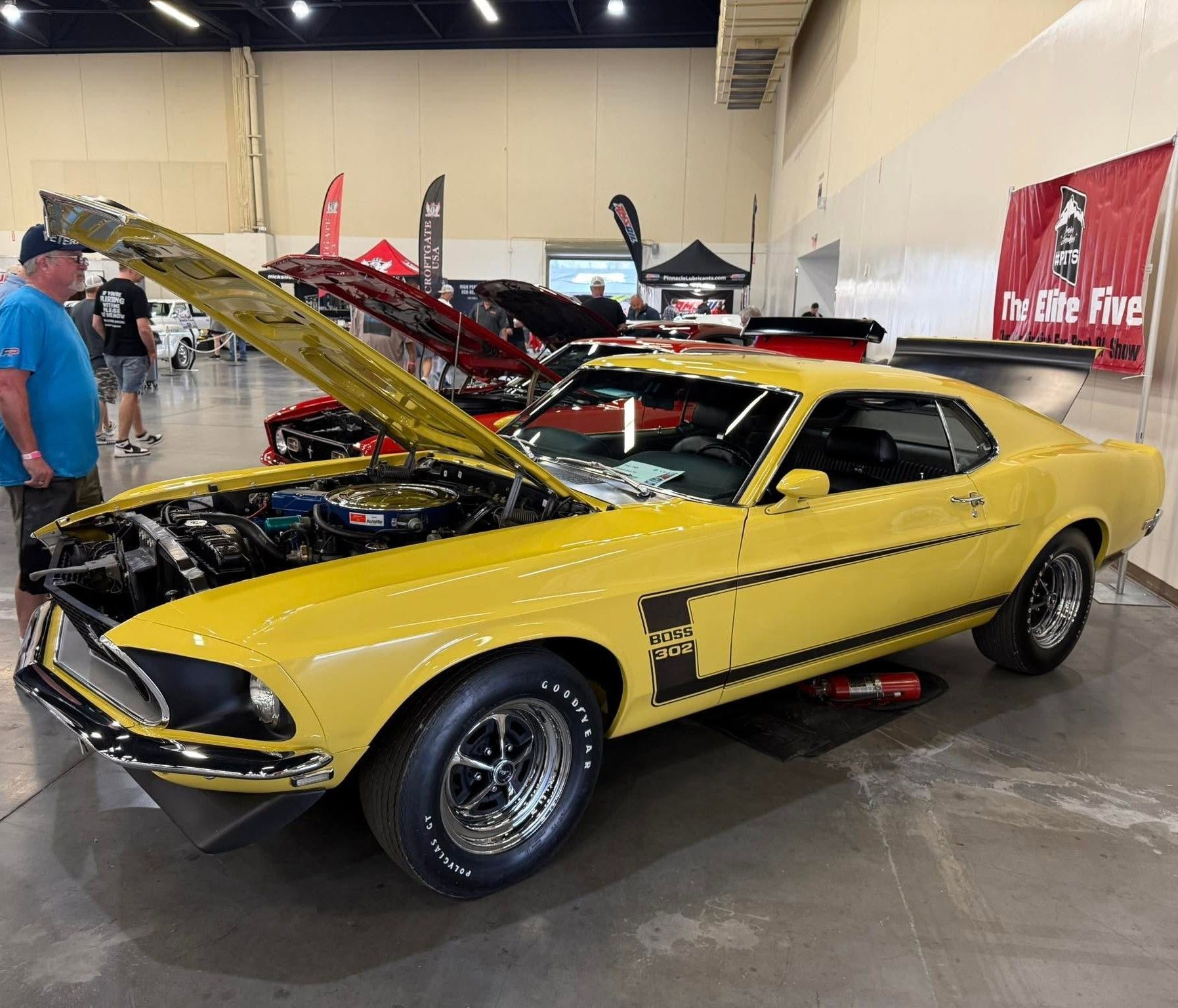 Yellow classic muscle car with hood open at an indoor car show