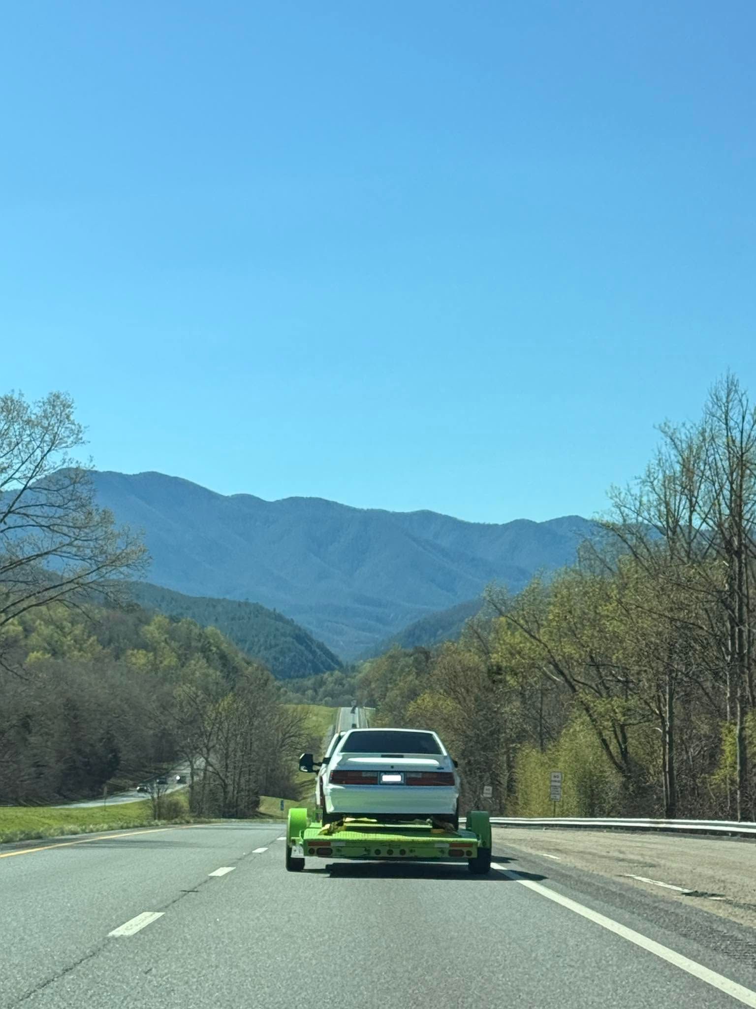 Green sports car on a mountain road with trees and hills under a clear blue sky