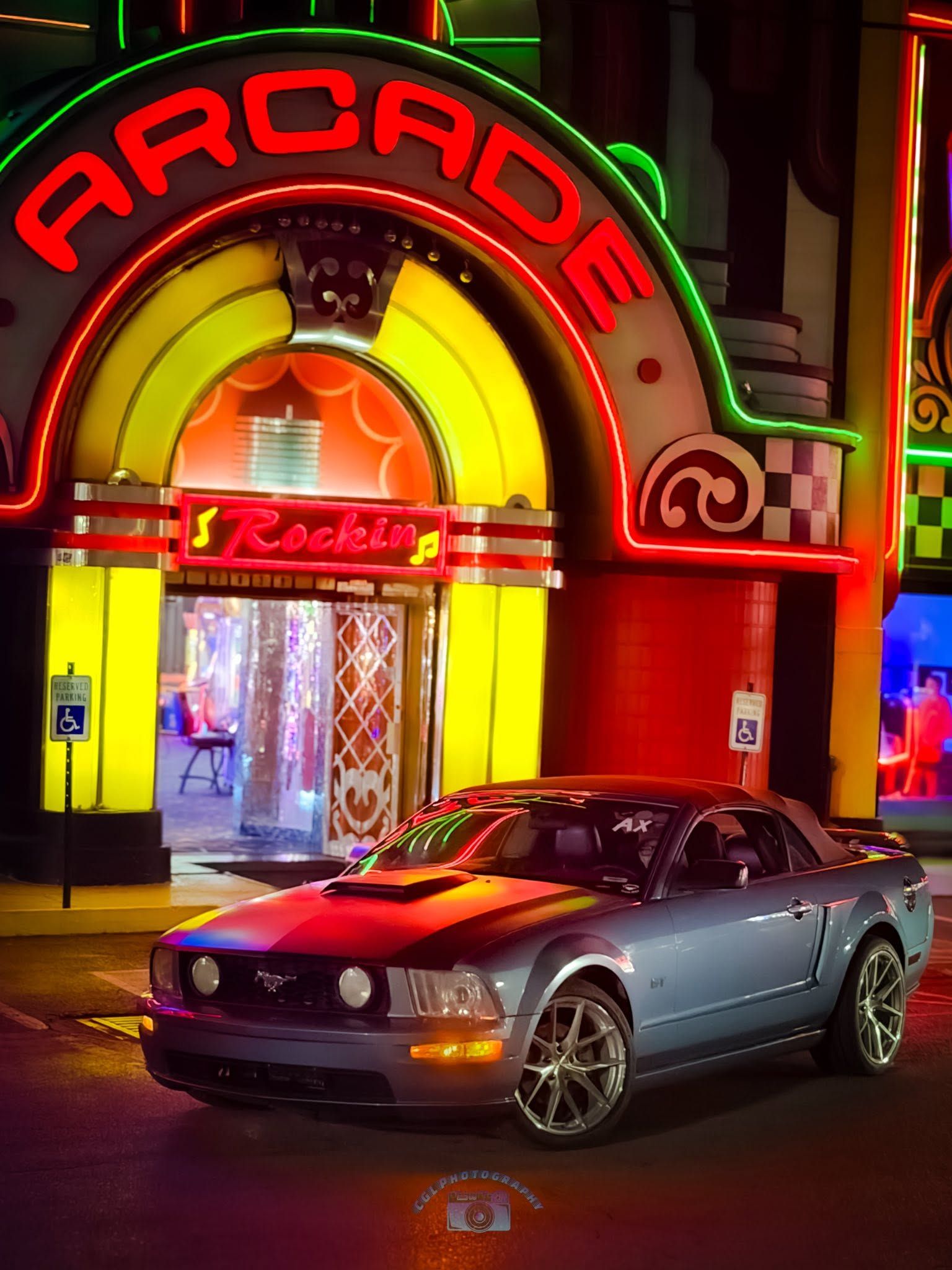 Gray sports car parked outside a neon-lit arcade entrance at night