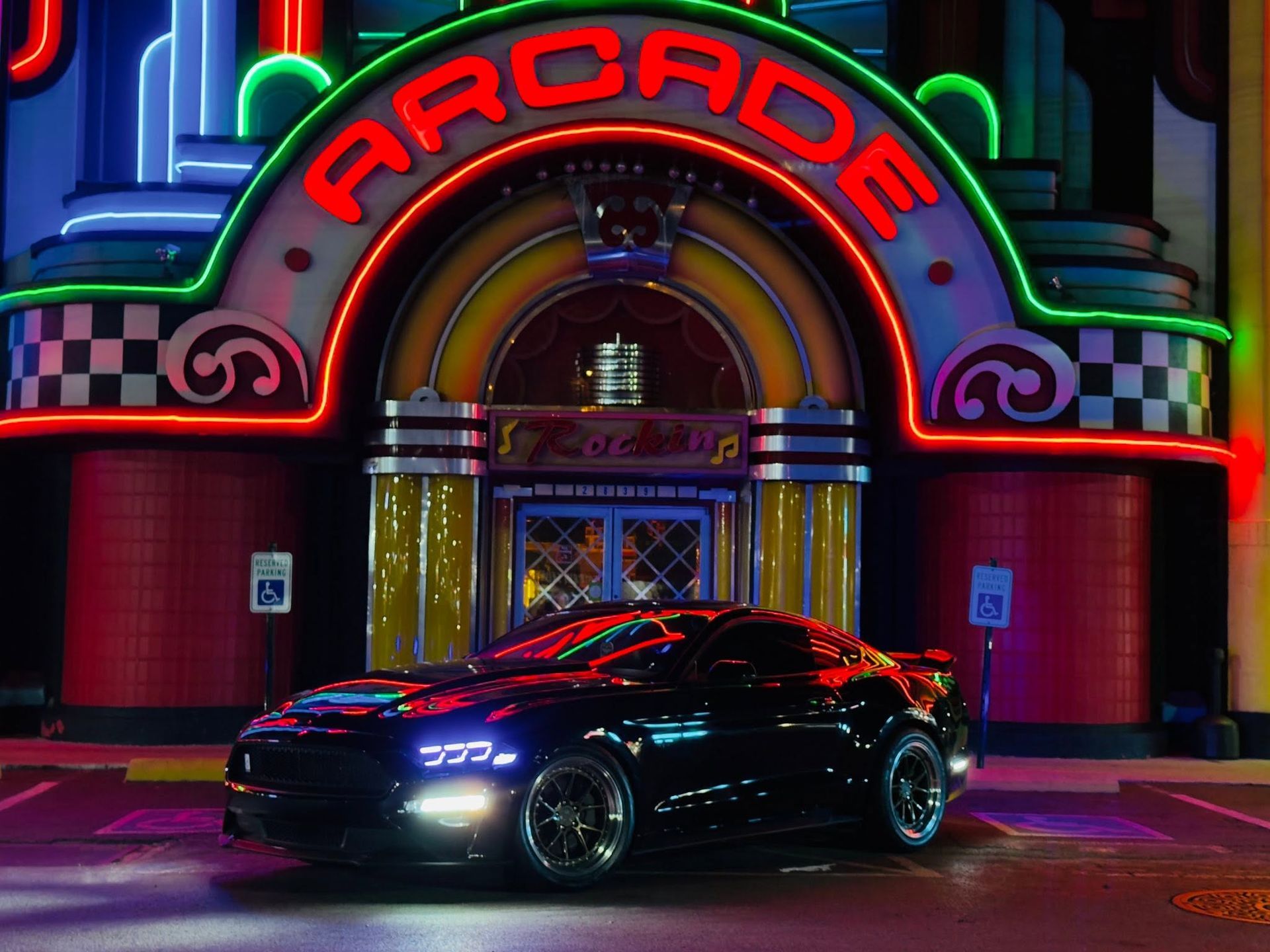 Black sports car parked outside a neon-lit arcade entrance at night