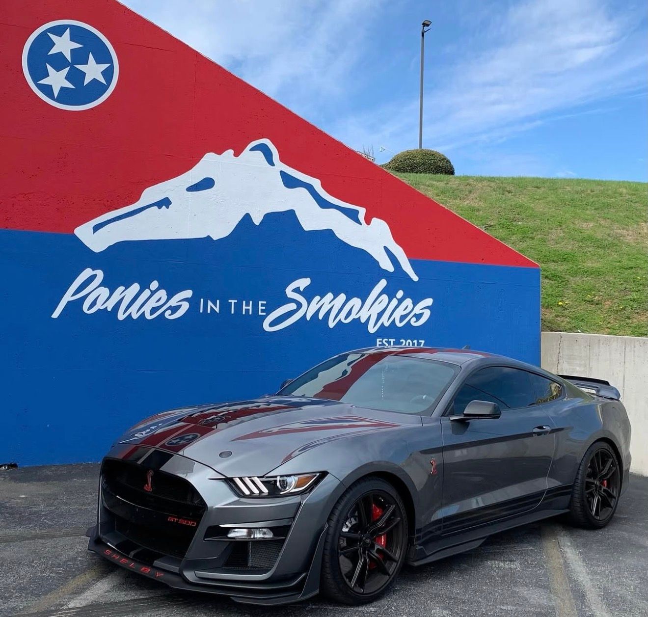 Gray sports car parked beside a colorful Pigeon Forge mural reading “Ponies in the Smokies.”