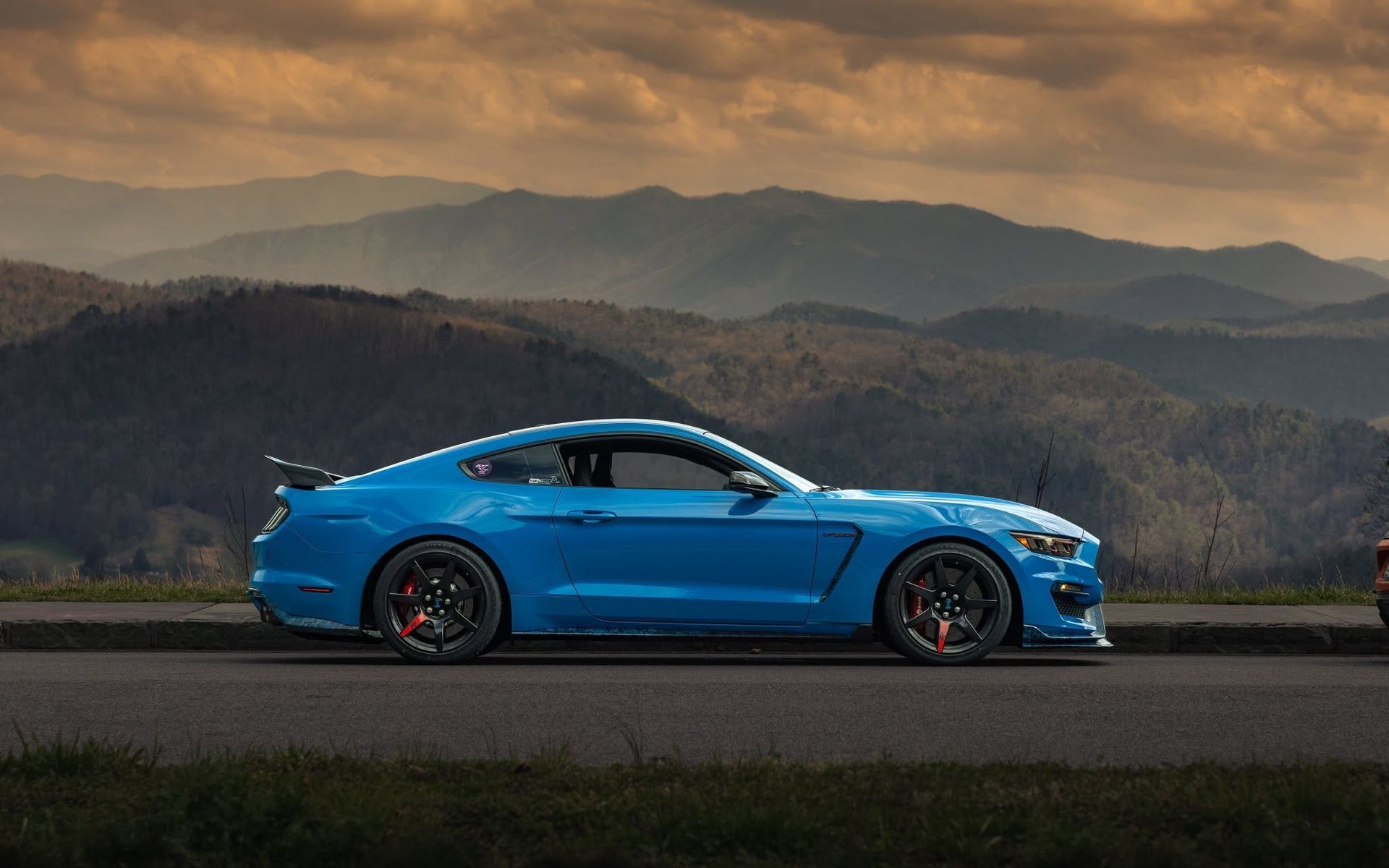 Blue sports car on a road with mountains in the background at sunset