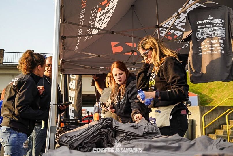 People at an outdoor booth arranging black T-shirts under a branded canopy.