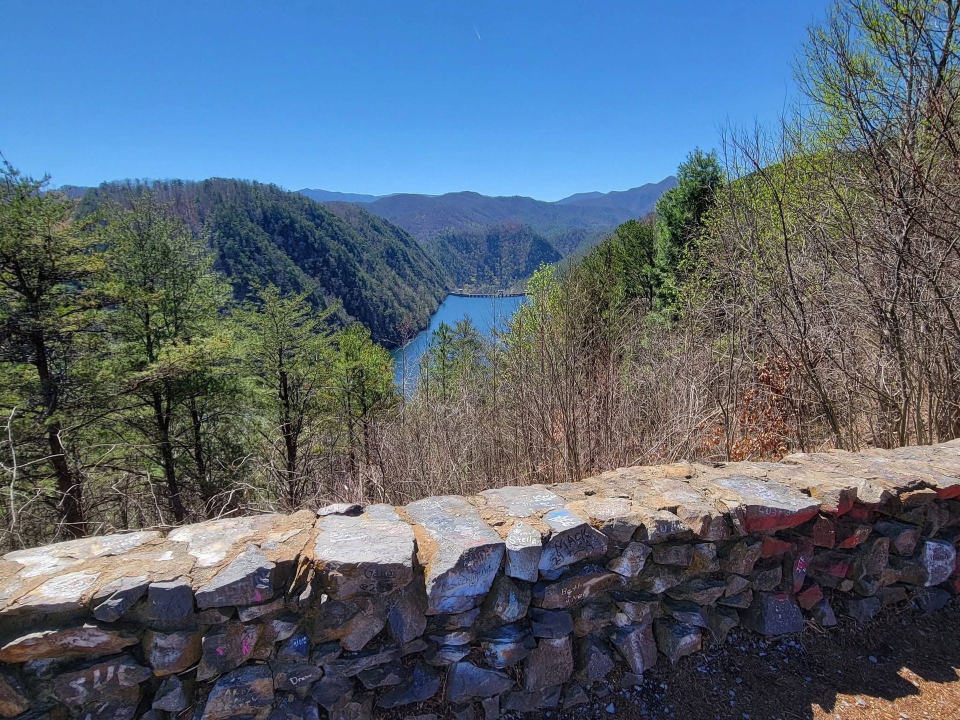 Stone wall overlooking a blue lake between green forested mountains under a clear sky