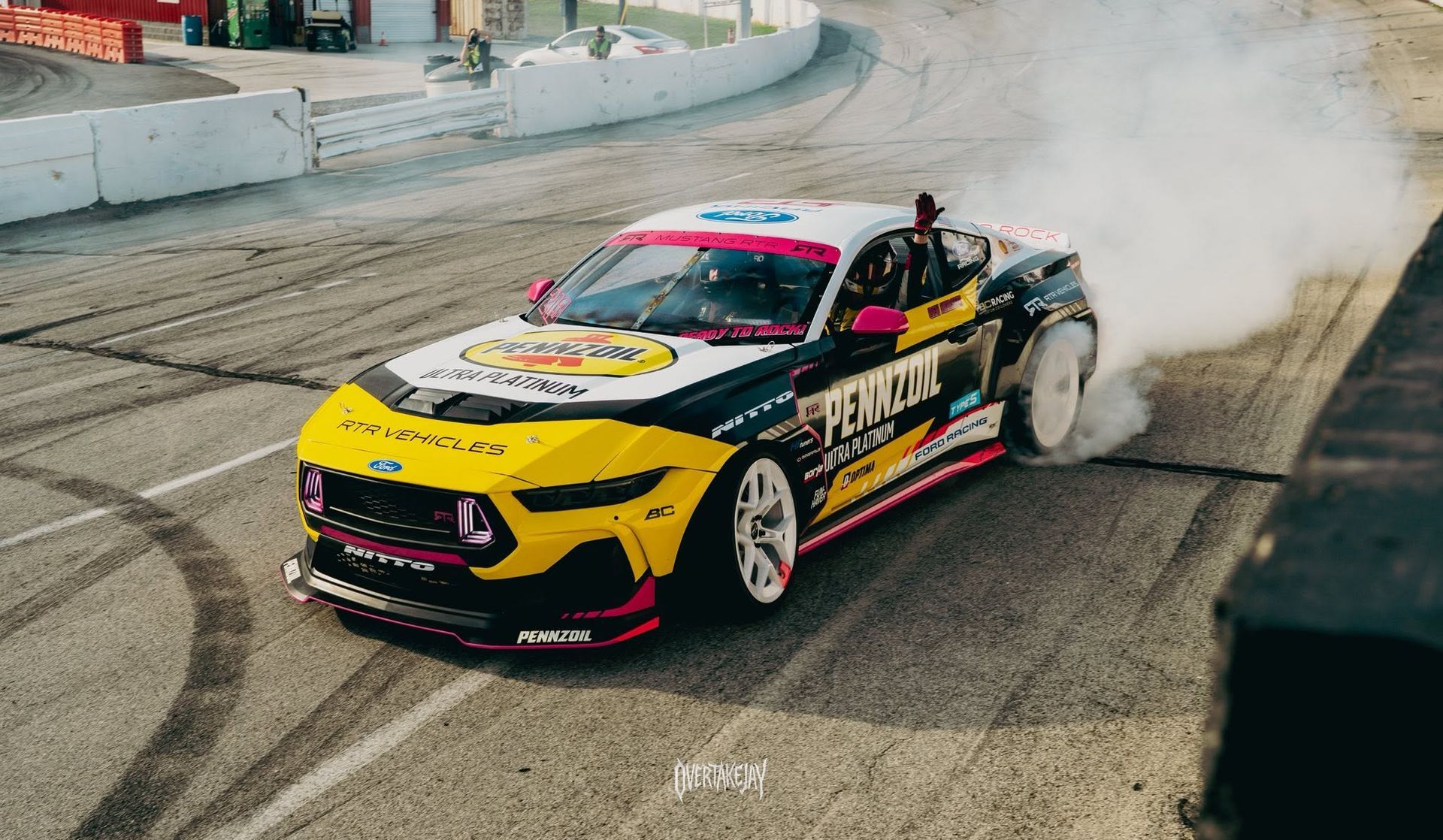 Drifting race car in yellow, black, and pink, smoking tires on a track