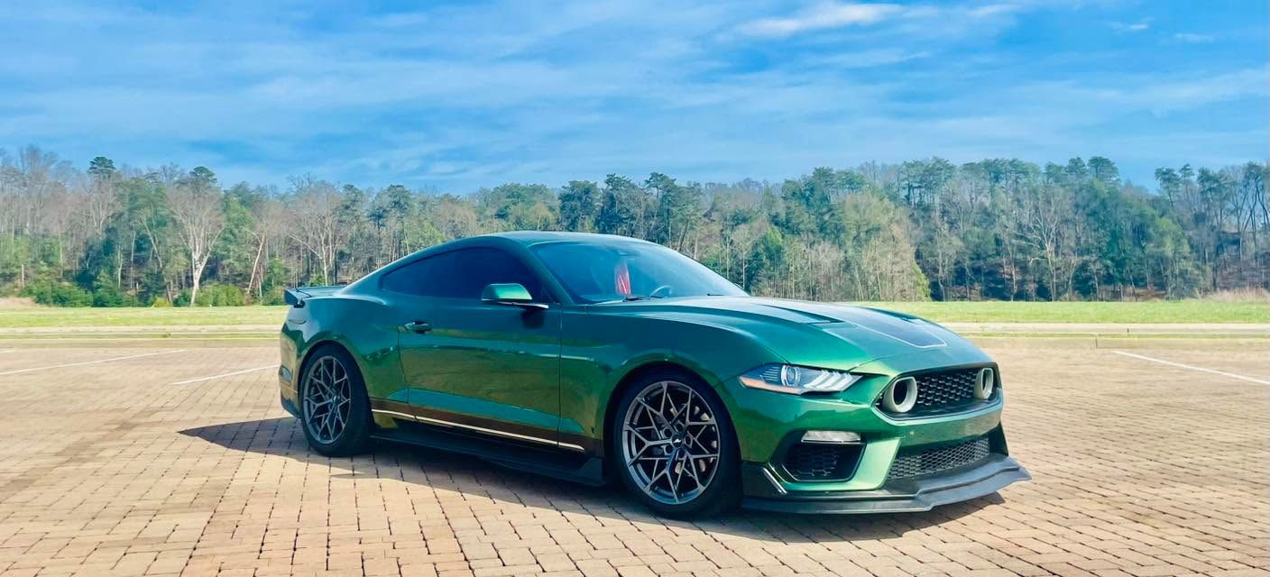 Green sports car parked on a brick path with trees and sky in the background