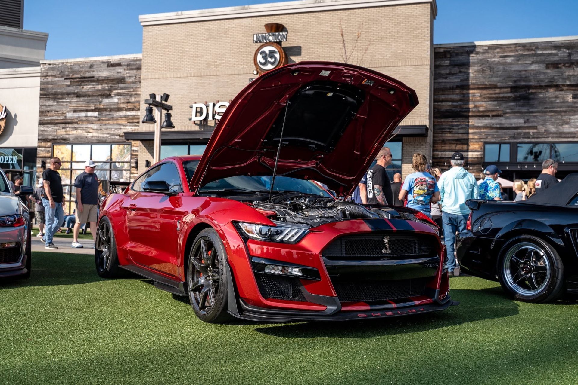 Red sports car with hood open at an outdoor car show crowd