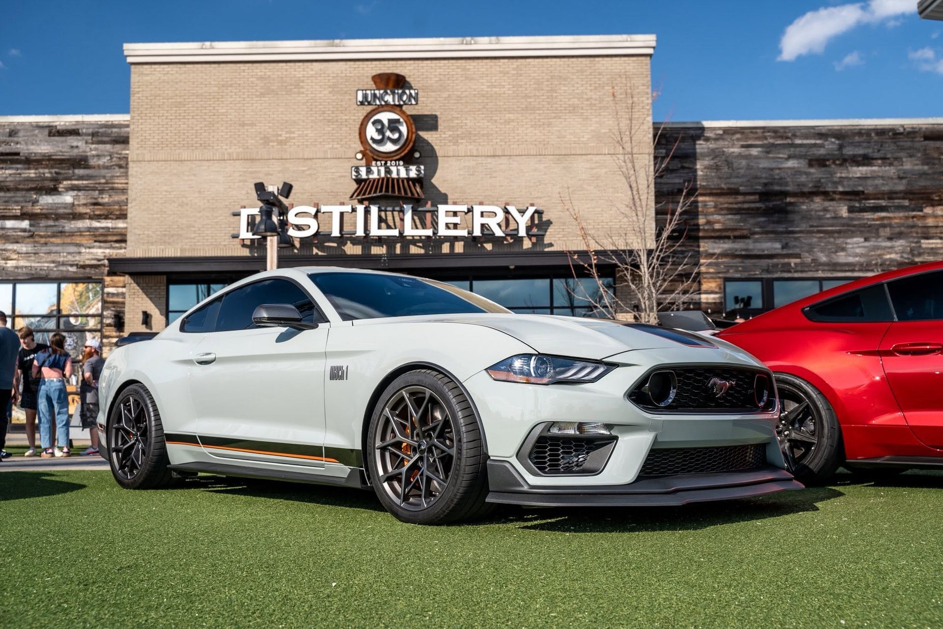 White sports car parked outside The Distillery with a red car beside it under a blue sky