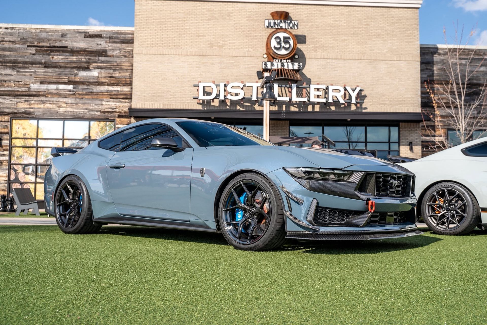 Silver sports car parked outside a distillery building on green grass.