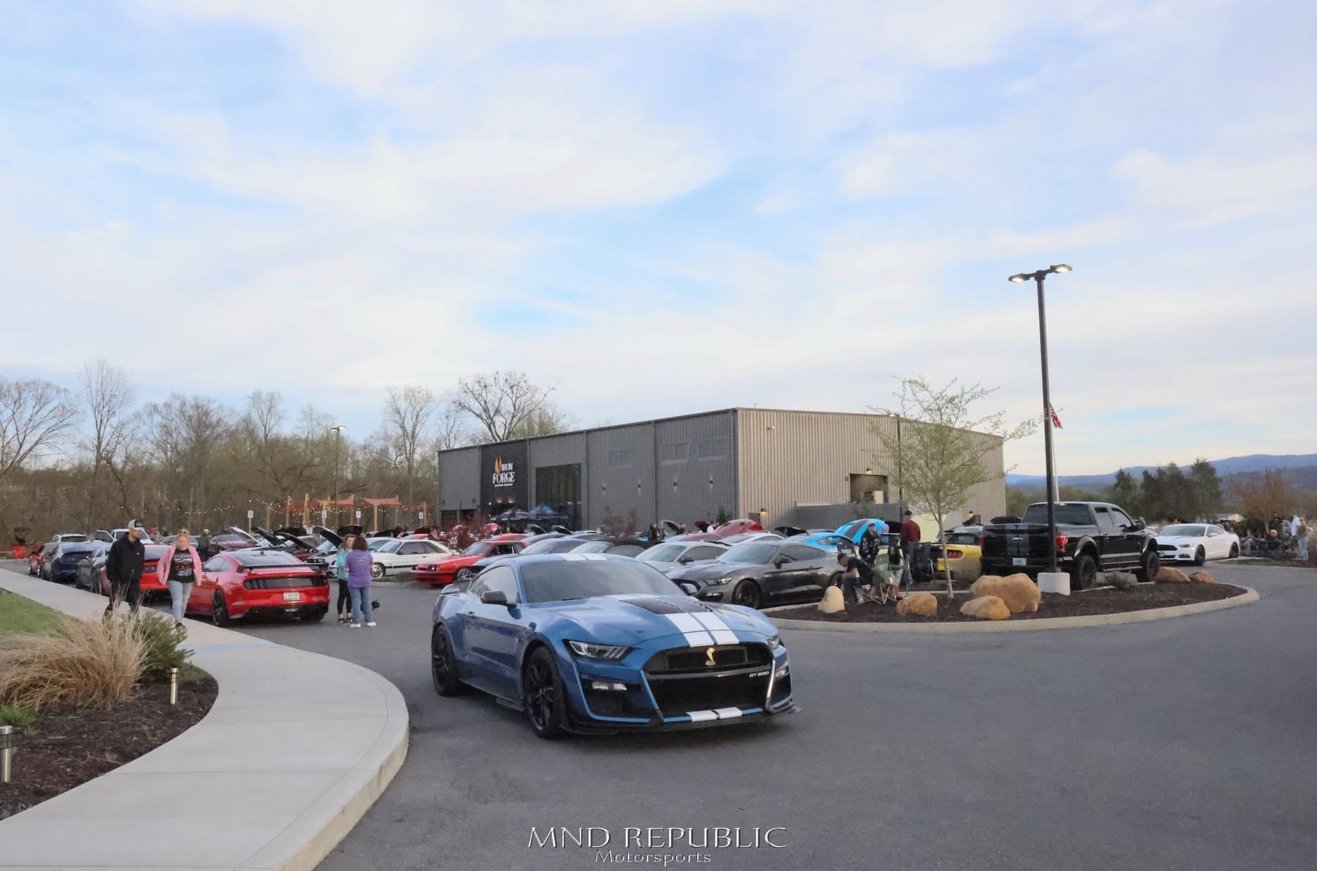 Classic sports cars lined up outside a building at a car meet on a cloudy day