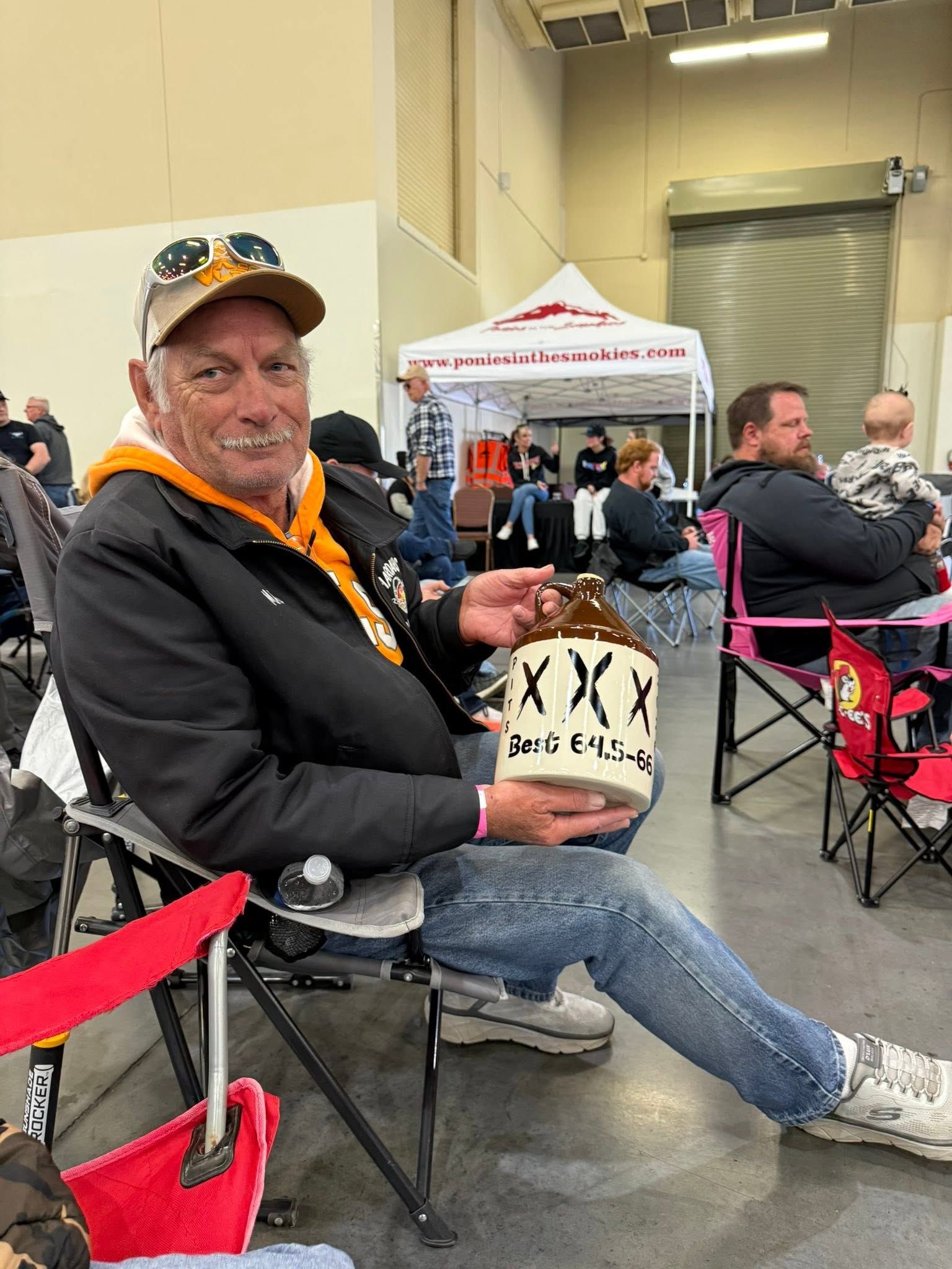 Seated man in orange cap holding a boxed item at an indoor event booth