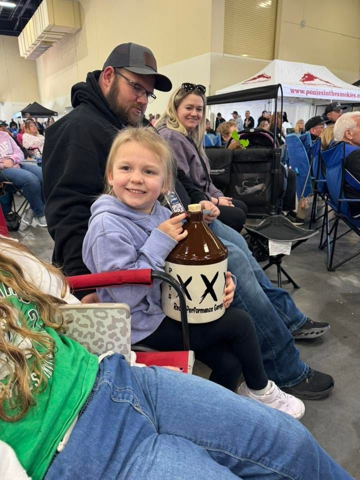 Child smiling in a crowd, holding a brown lantern-style cup at an outdoor event.