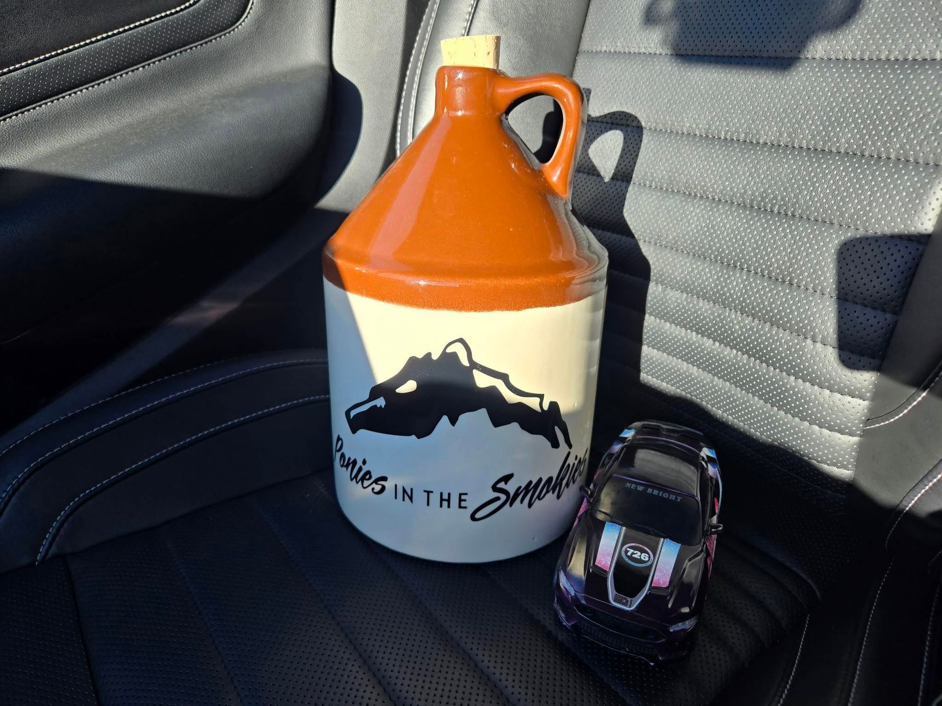 Orange-and-white jug with mountain logo beside a small watch on a car seat