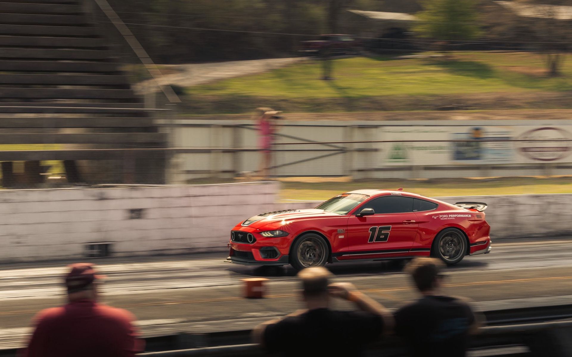 Red race car speeding on a track, with blurred spectators in the foreground.