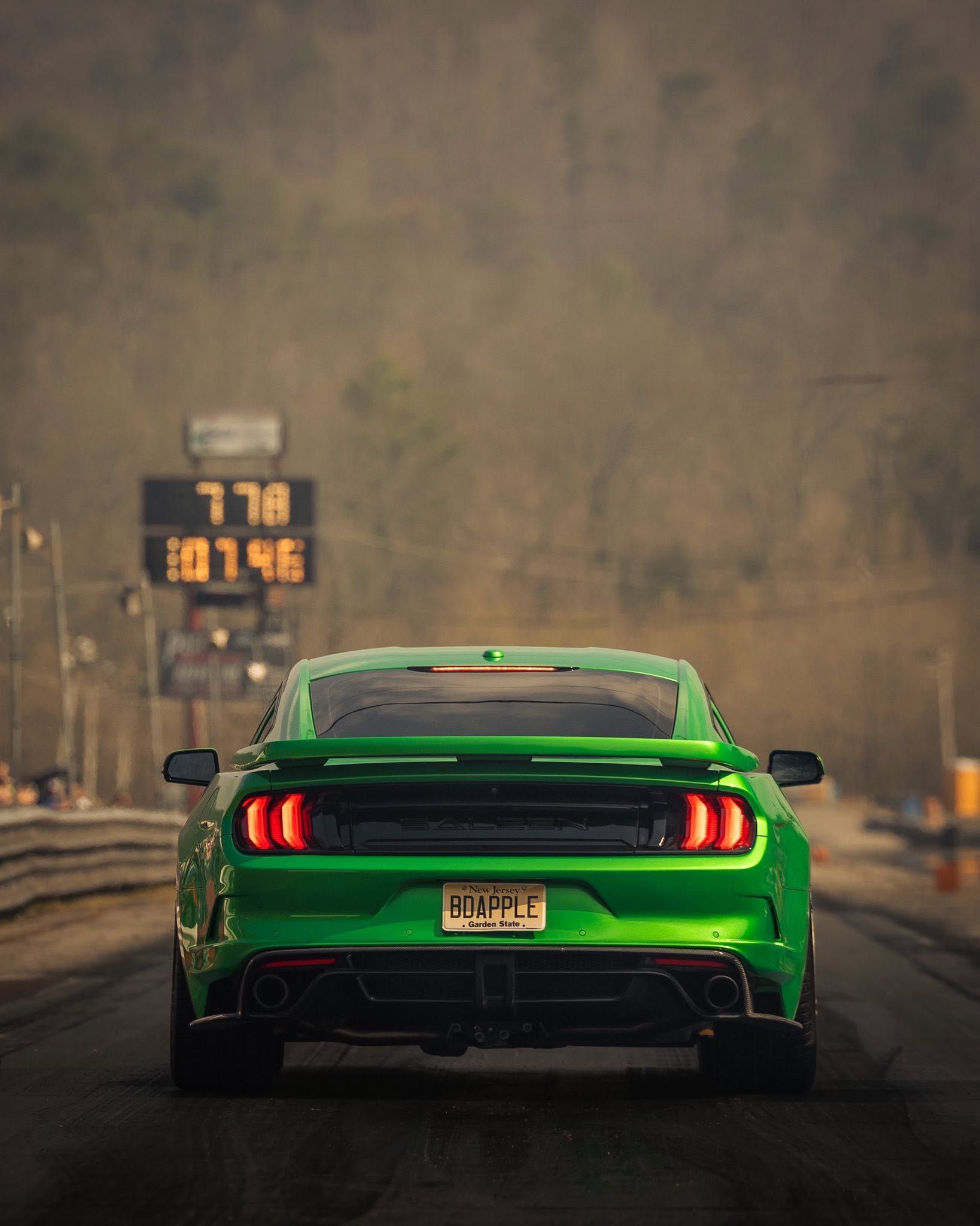 Green sports car racing down a track, seen from behind, with a digital scoreboard on the left.