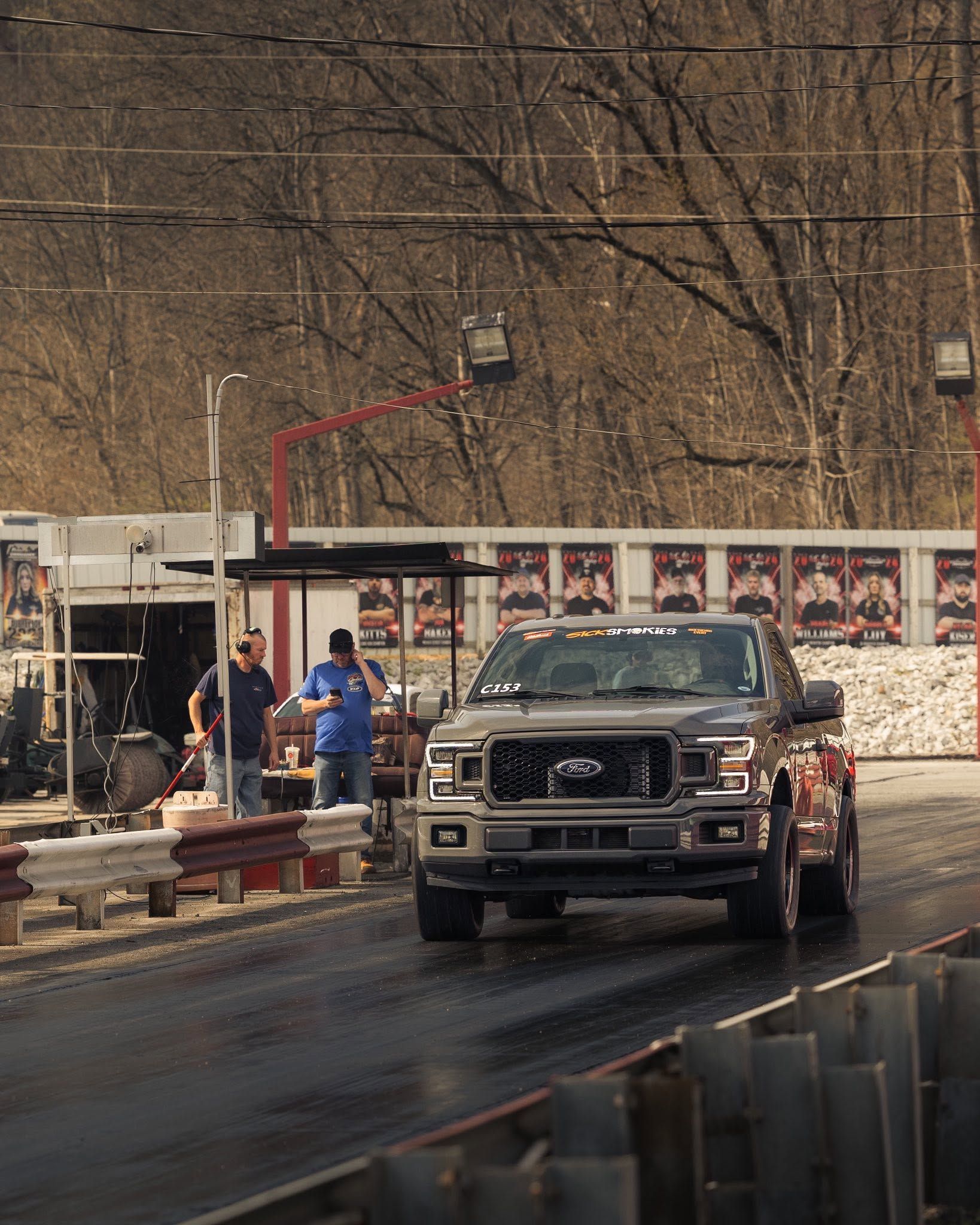 Tow truck on a wet road near a roadside barrier, with people standing by in winter scenery.