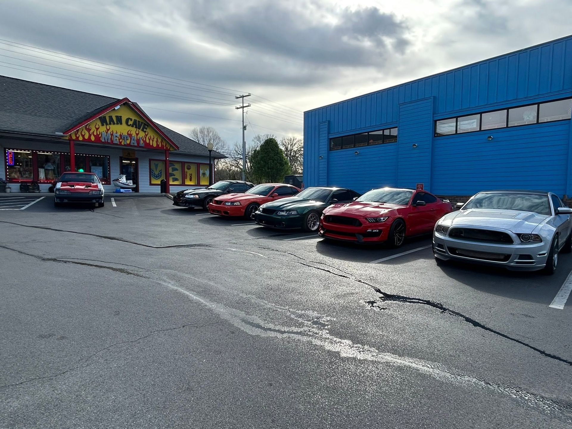 Car lot outside a blue building with several parked cars under a cloudy sky