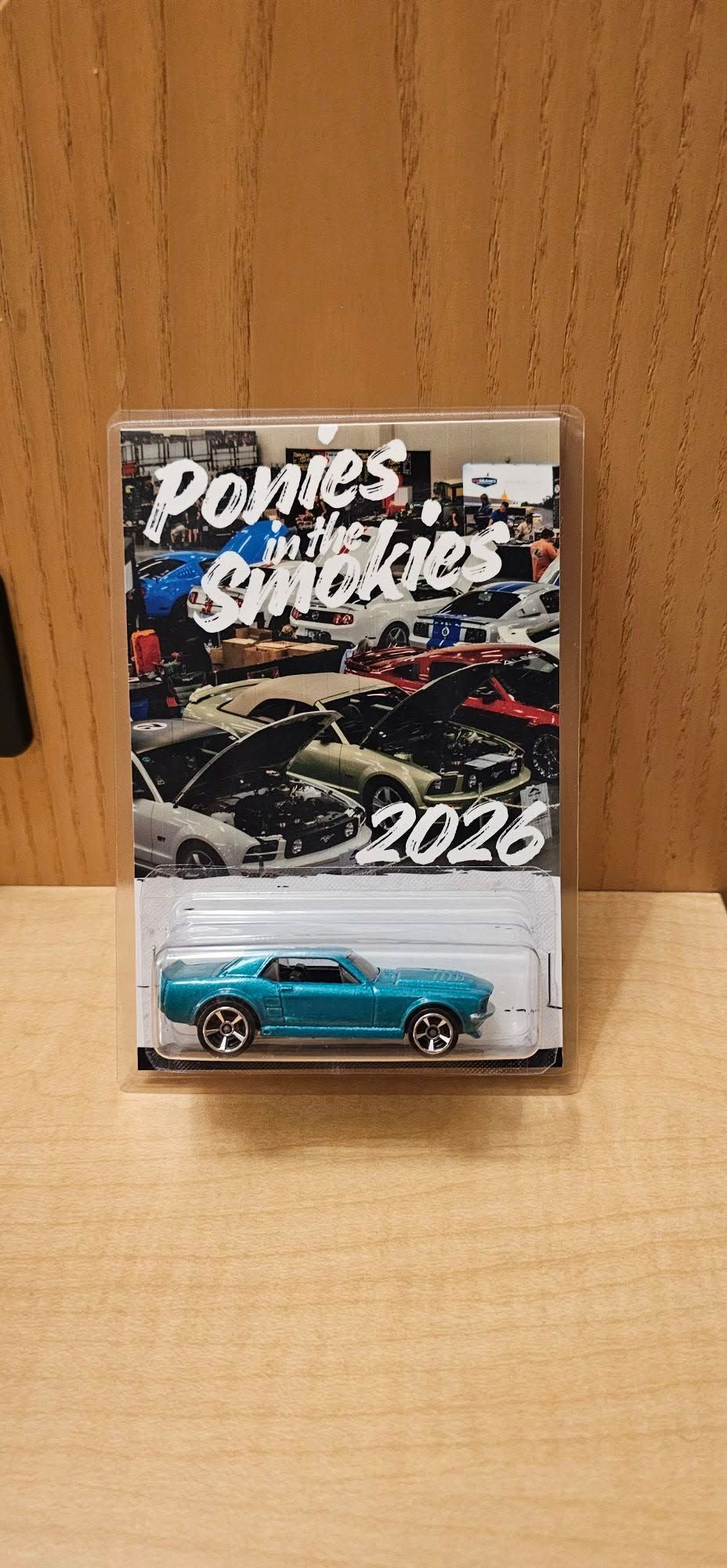 Blue toy car in a clear display case on a wooden surface, with a 