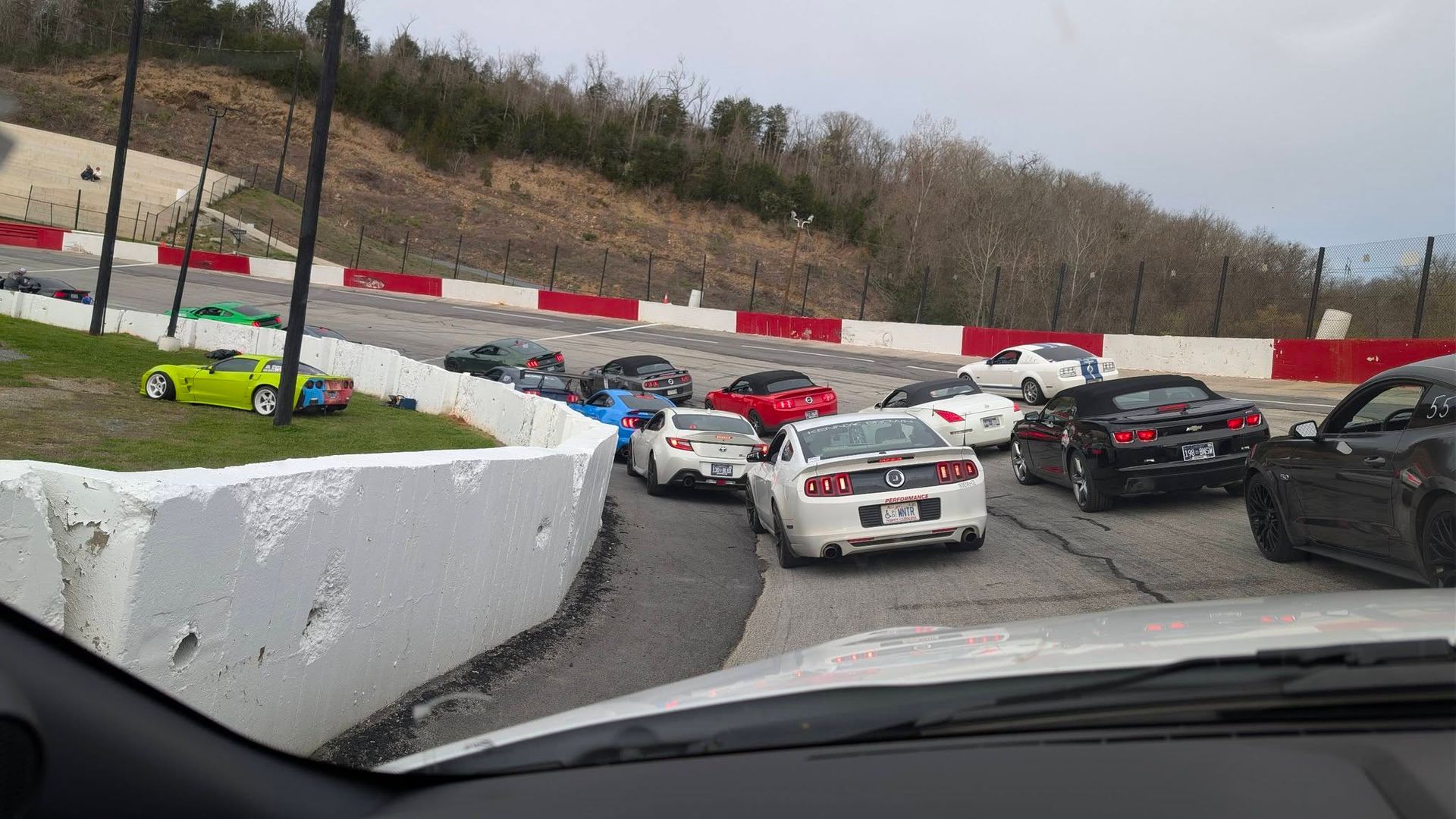 Race cars piled up on a wet track, viewed from a car at a sharp turn with barriers and woods nearby
