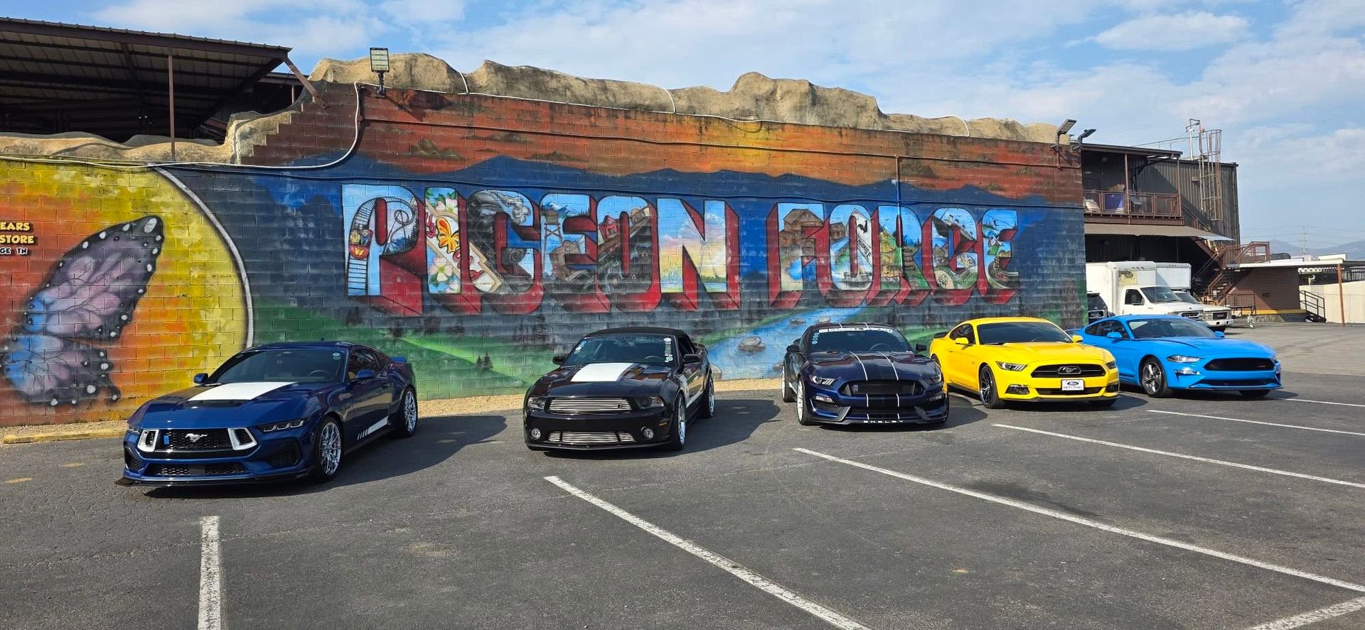 Five sports cars parked in front of a colorful mural reading “RICEEN RIDE”