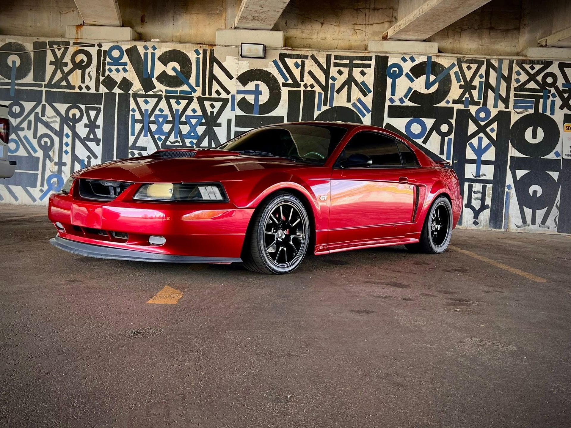 Red sports coupe parked under a bridge with black-and-white graffiti on the wall behind it