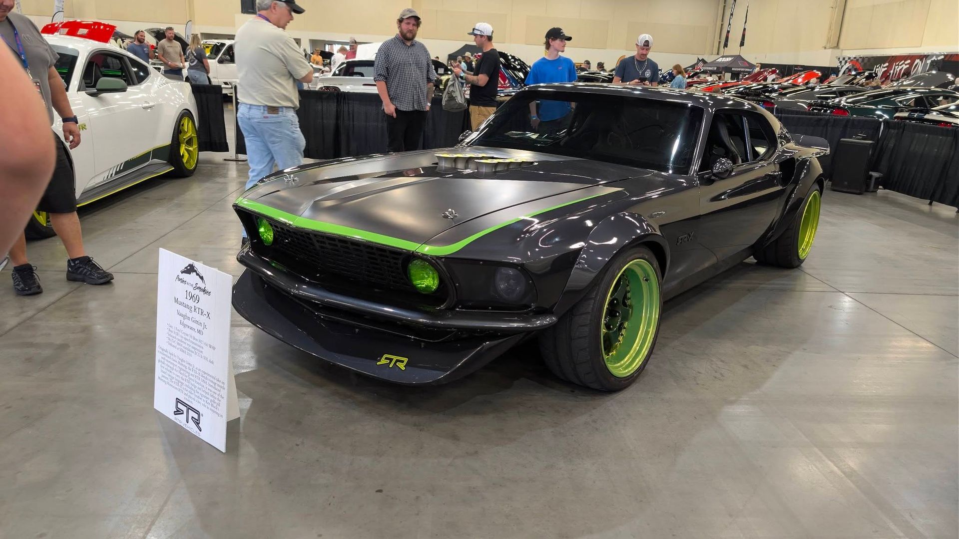 Black classic muscle car with neon green rims on display at an indoor car show